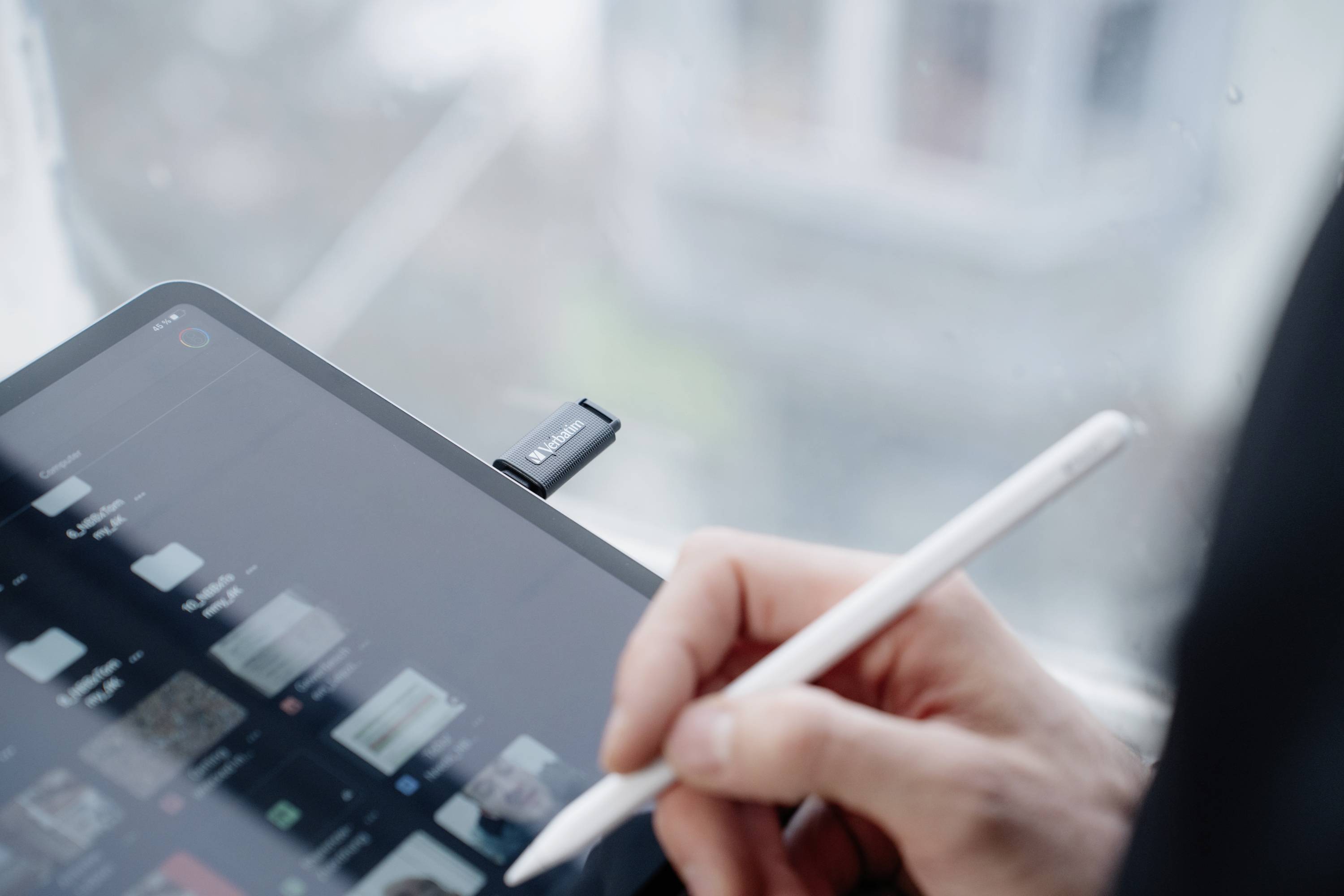 A person is writing with a pen on a tablet that is lying on a table. A USB stick is connected to the tablet.