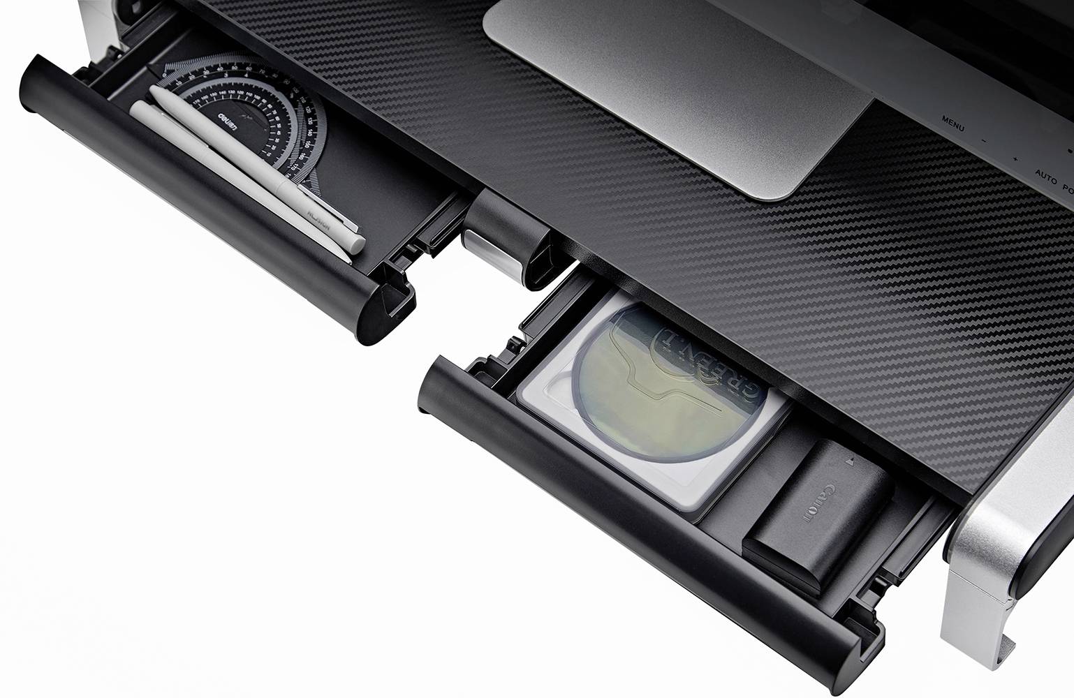 Two open drawers of a desk, with one on the left containing pens and a geometry set square, and the other on the right with a labelled envelope and a black device.