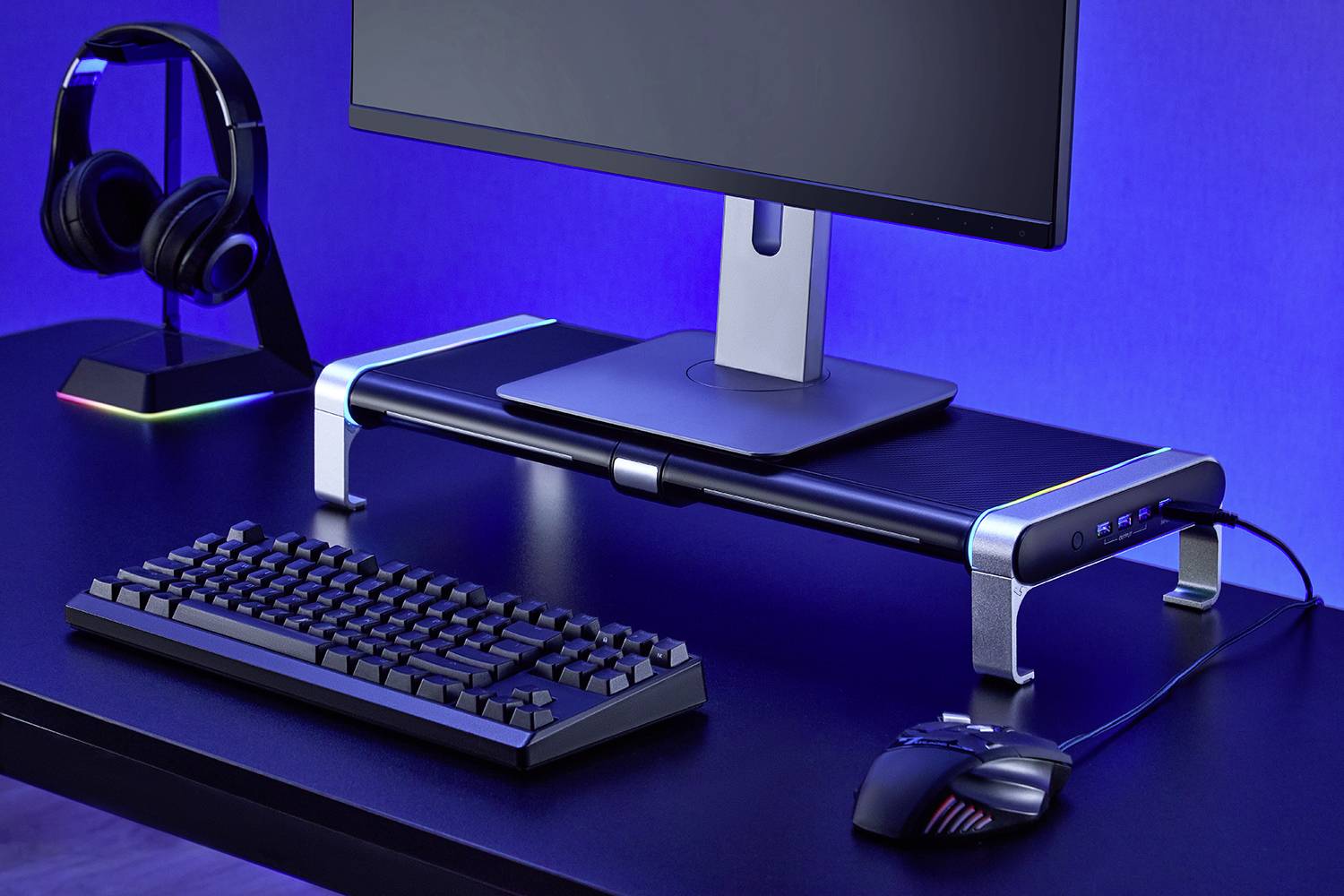 A computer workstation with a monitor on a raised stand, alongside a keyboard, mouse, and a headset on a stand.