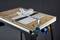 A table circular saw with a metal guide rail, safety guard, and wooden board on a black frame, ready for woodworking.
