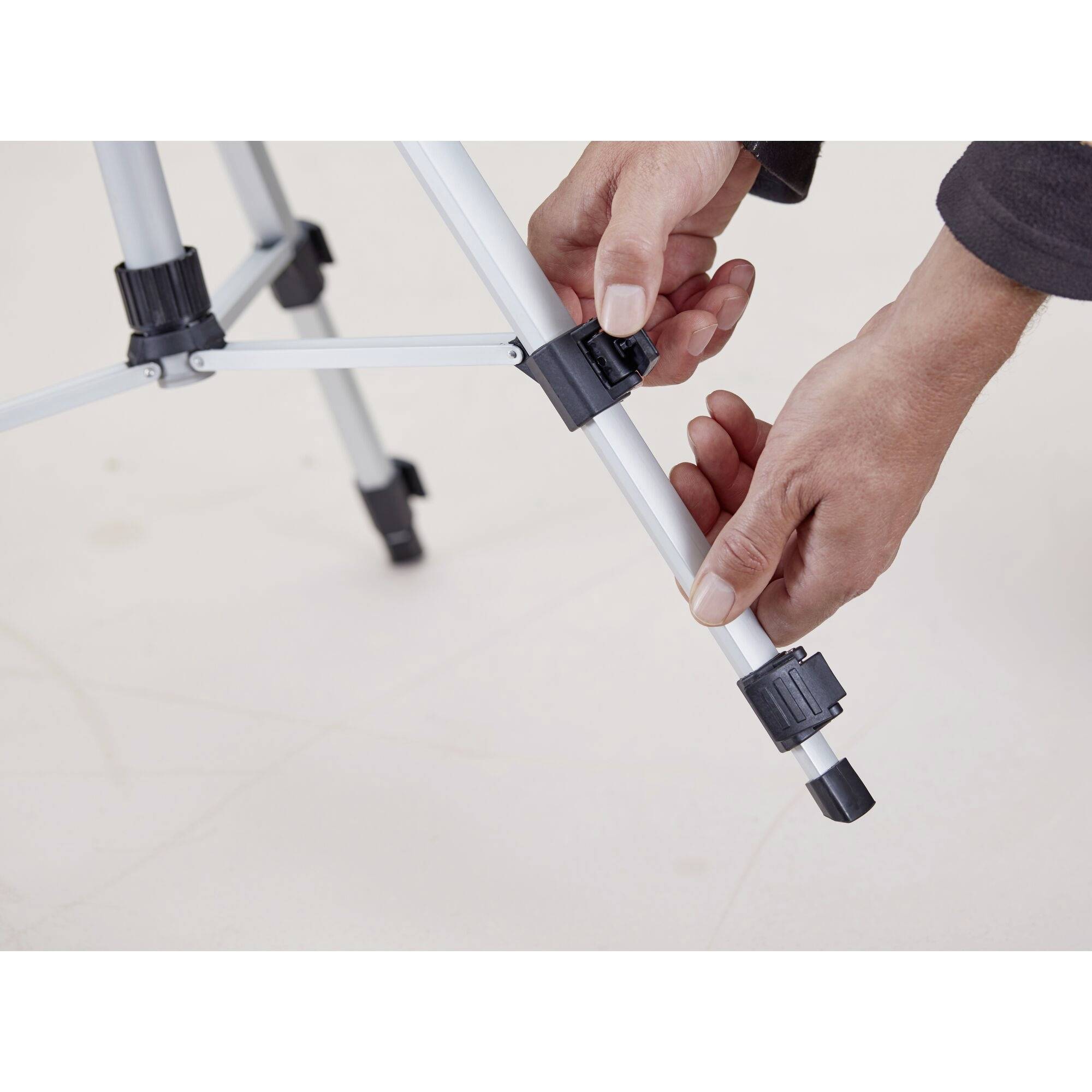A person adjusts the height of a tripod by opening a clamp on one of the legs.