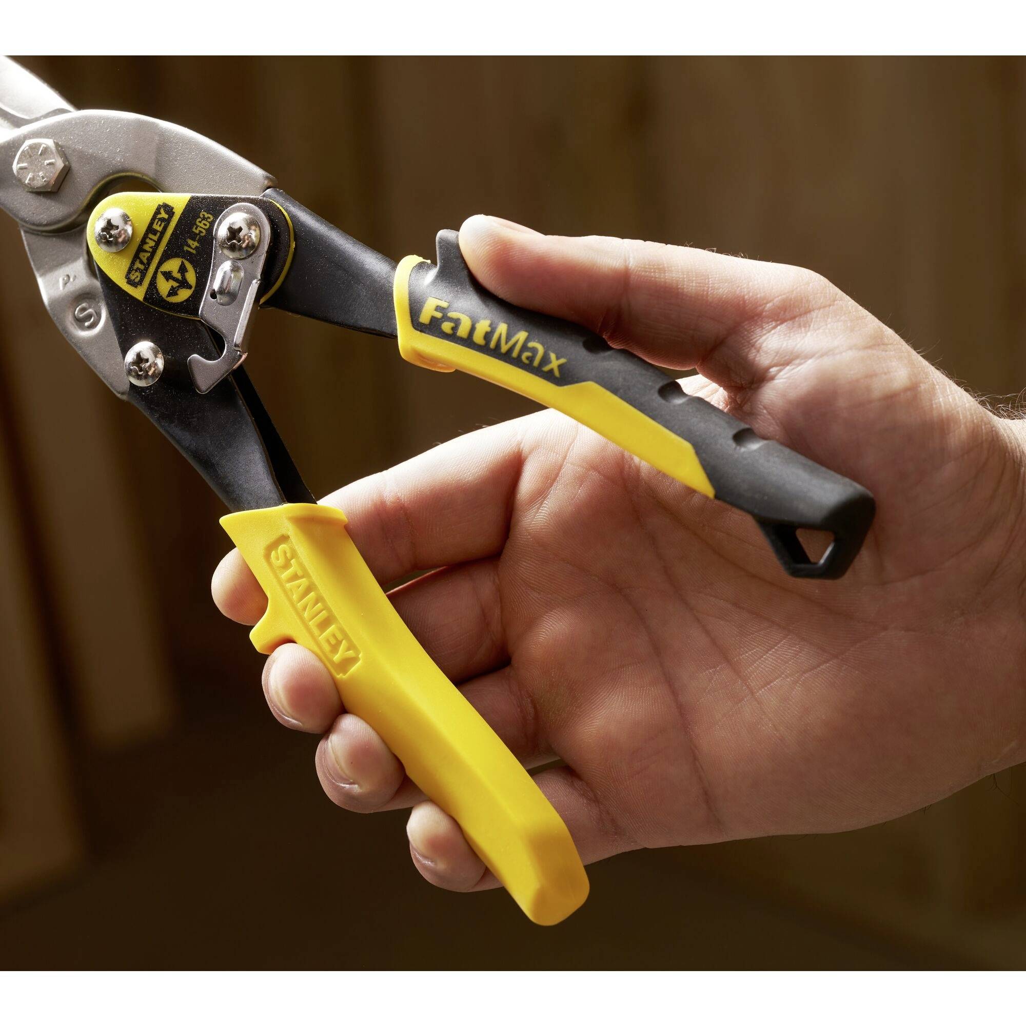 A hand is holding a yellow and black metal snips by the brand 'FatMax', suitable for cutting metal sheets.