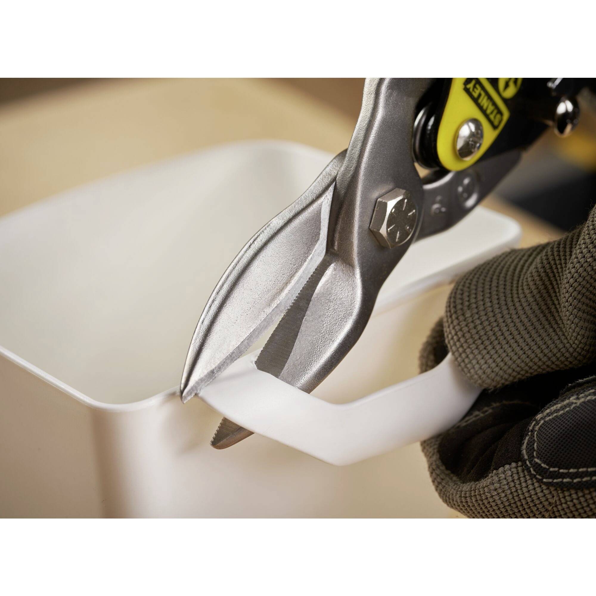 A metal scissors cuts through a thin white plastic stem. A gloved hand holds the handle.