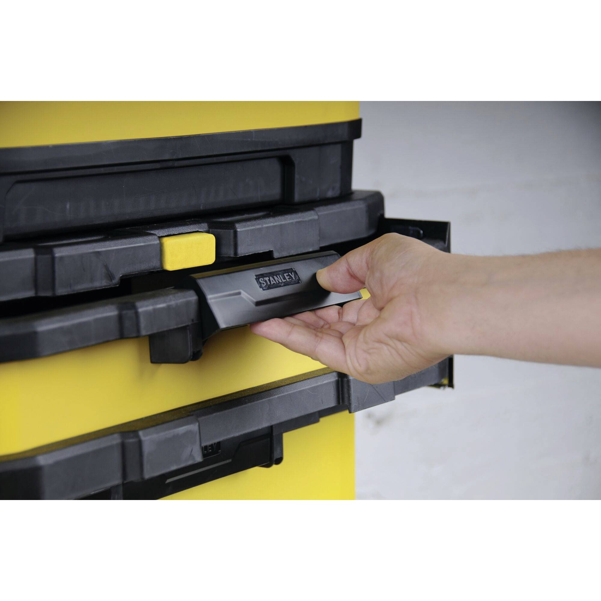 'A hand pulls out a drawer with a black handle from a yellow toolbox.'