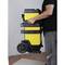 A person is transporting a yellow wheeled toolbox. The case has multiple stackable compartments and is carried at its side.