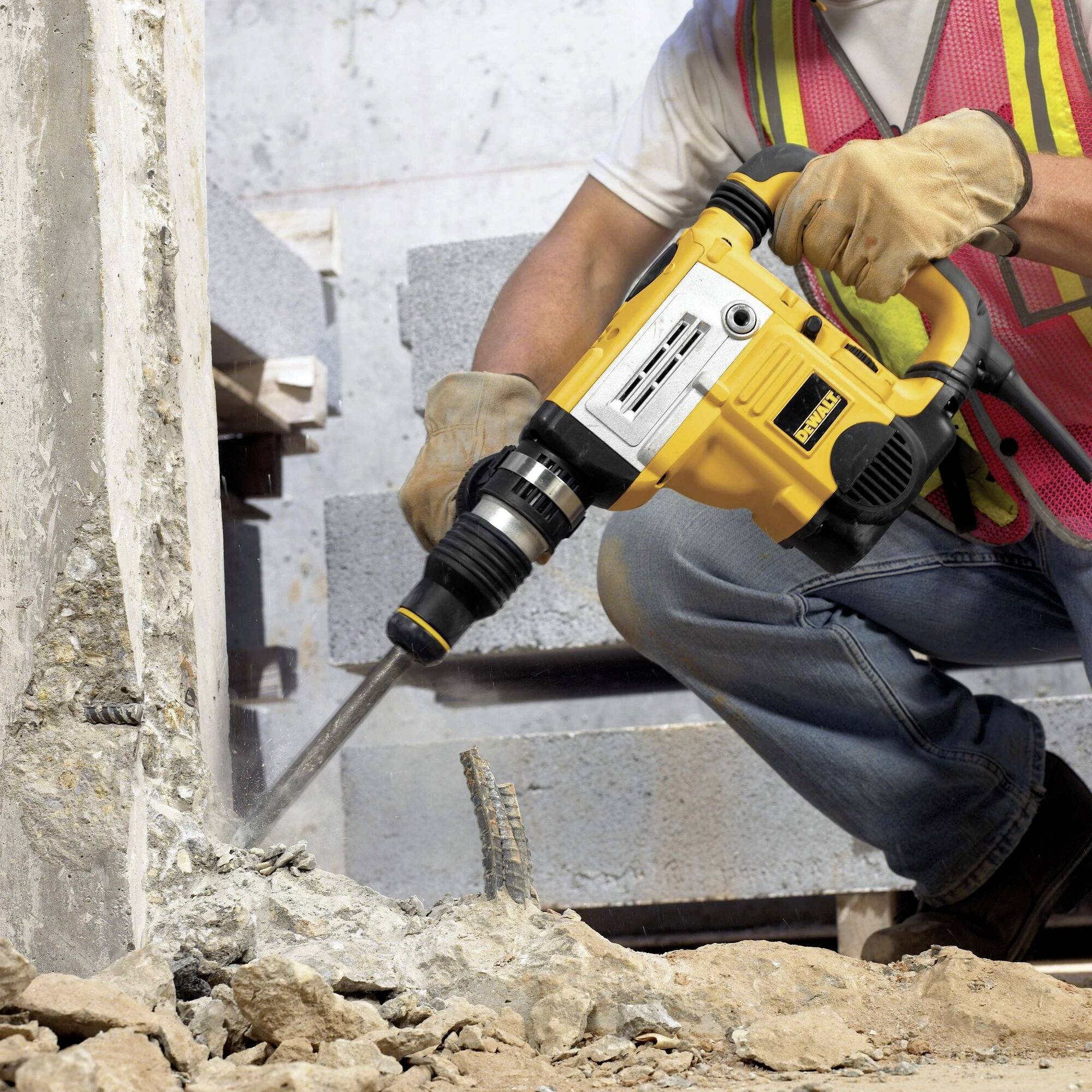 A person is using a yellow hammer drill to work on concrete. They are wearing safety clothing and gloves.