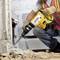 A person is using a yellow hammer drill to work on concrete. They are wearing safety clothing and gloves.