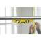 A yellow spirit level rests on a metal pipe, with a blurry person holding a tape measure against the wall in the background.