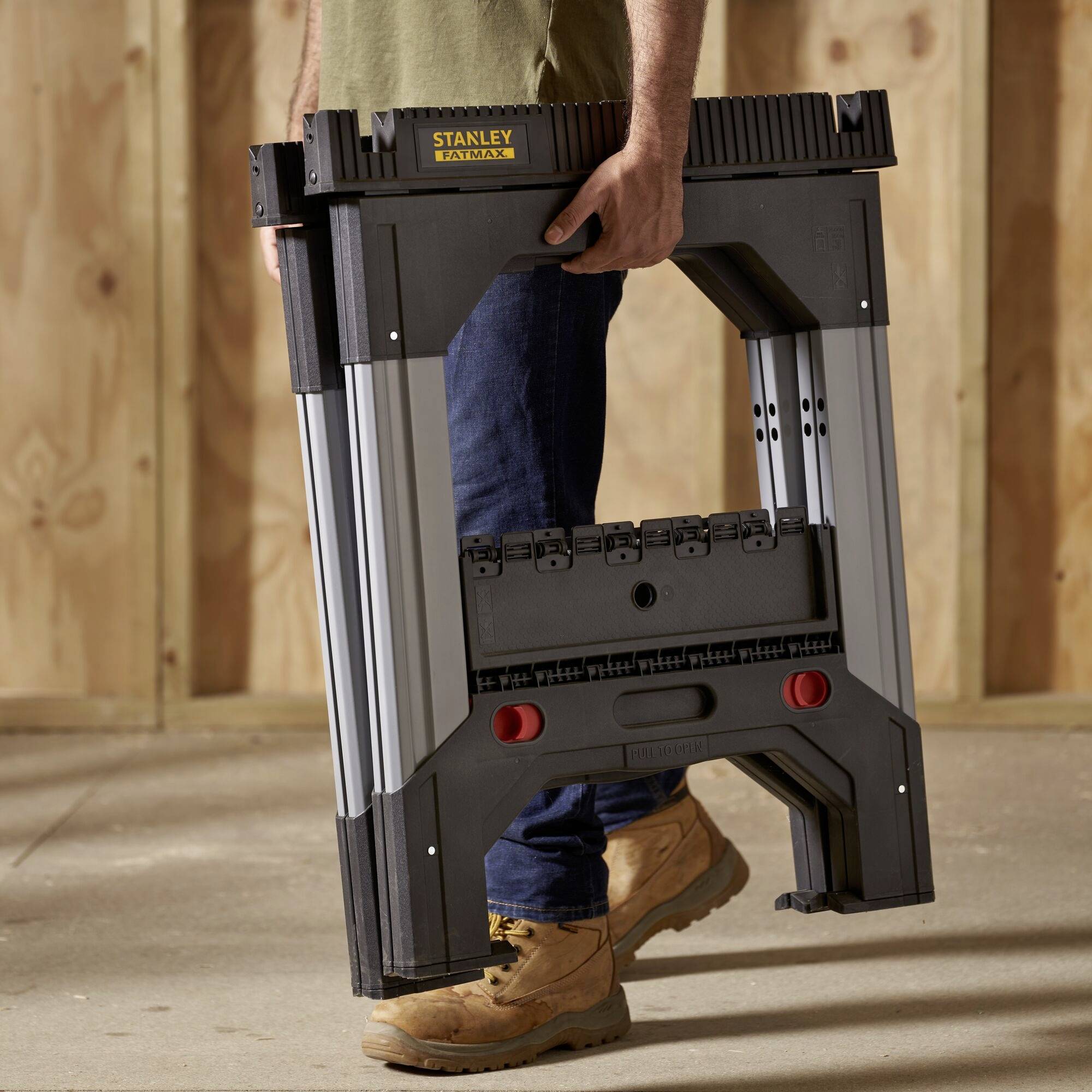 A person is holding a portable, folding work table by Stanley in a woodworking workshop.