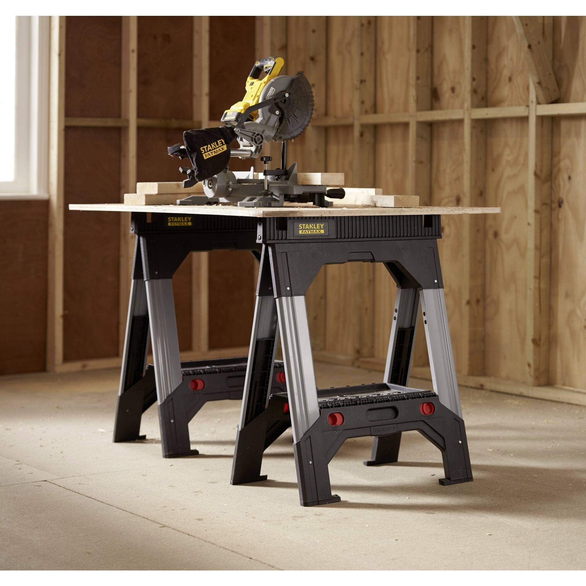 Workshop with a circular saw on a portable workbench in an unfinished room. Surrounded by unclad wooden walls.