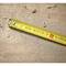 A yellow tape measure lies diagonally on a surface with wood dust and shavings, indicating woodworking activities.