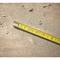 Yellow tape measure on a dusty wooden floor with wood shavings, indicating a craftsman's or construction environment.
