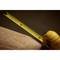 A yellow measuring tape is stretched across a wooden table with wood shavings, showing precise centimetre and inch markings.
