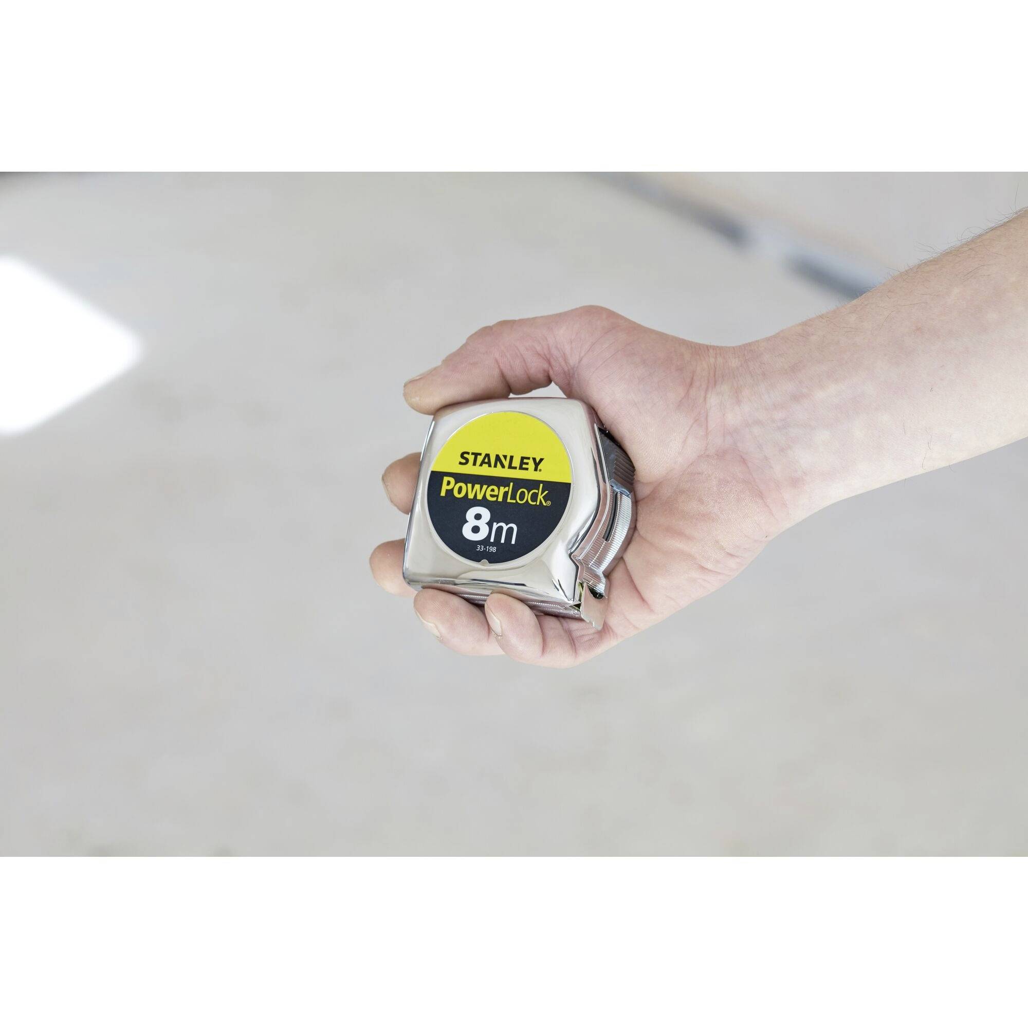 A hand is holding an 8-metre Stanley PowerLock measuring tape.
