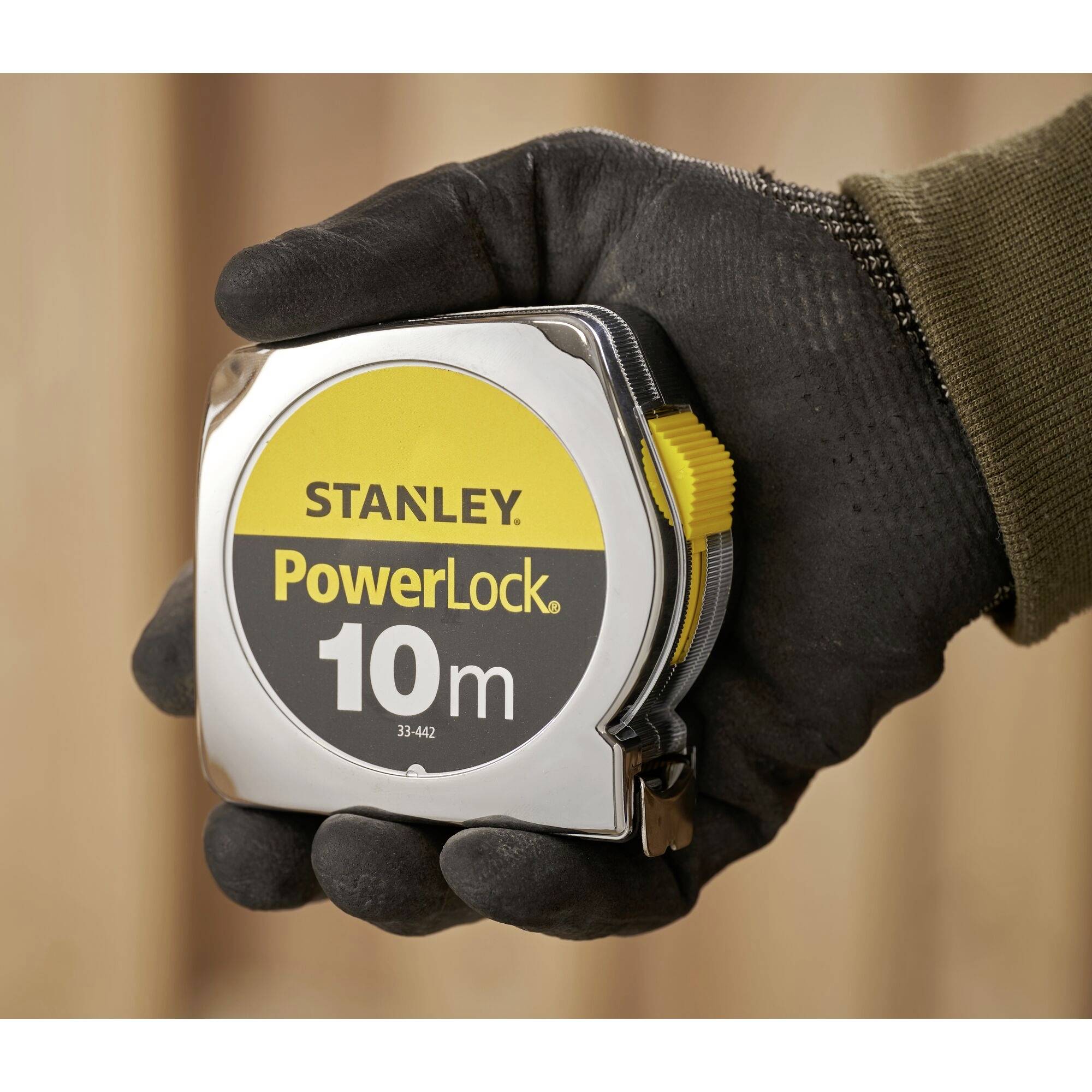 A person is holding a Stanley 'PowerLock' tape measure that can measure 10 metres. It is being held in a gloved hand.