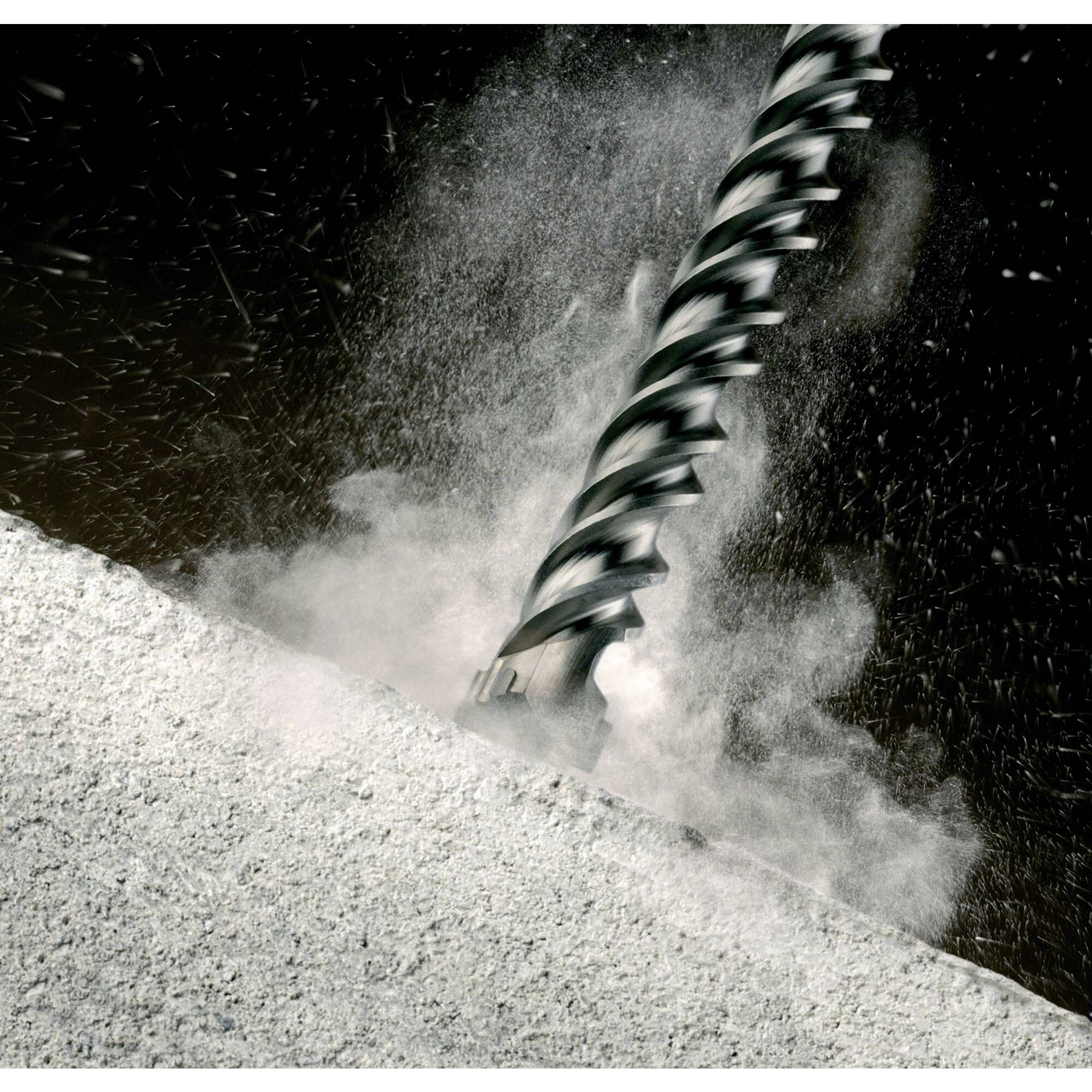 Drill penetrates concrete, dust cloud forms.