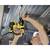 A person is drilling into the ceiling of a building with a yellow drill. Surrounded by pipes and tunnel conduits.