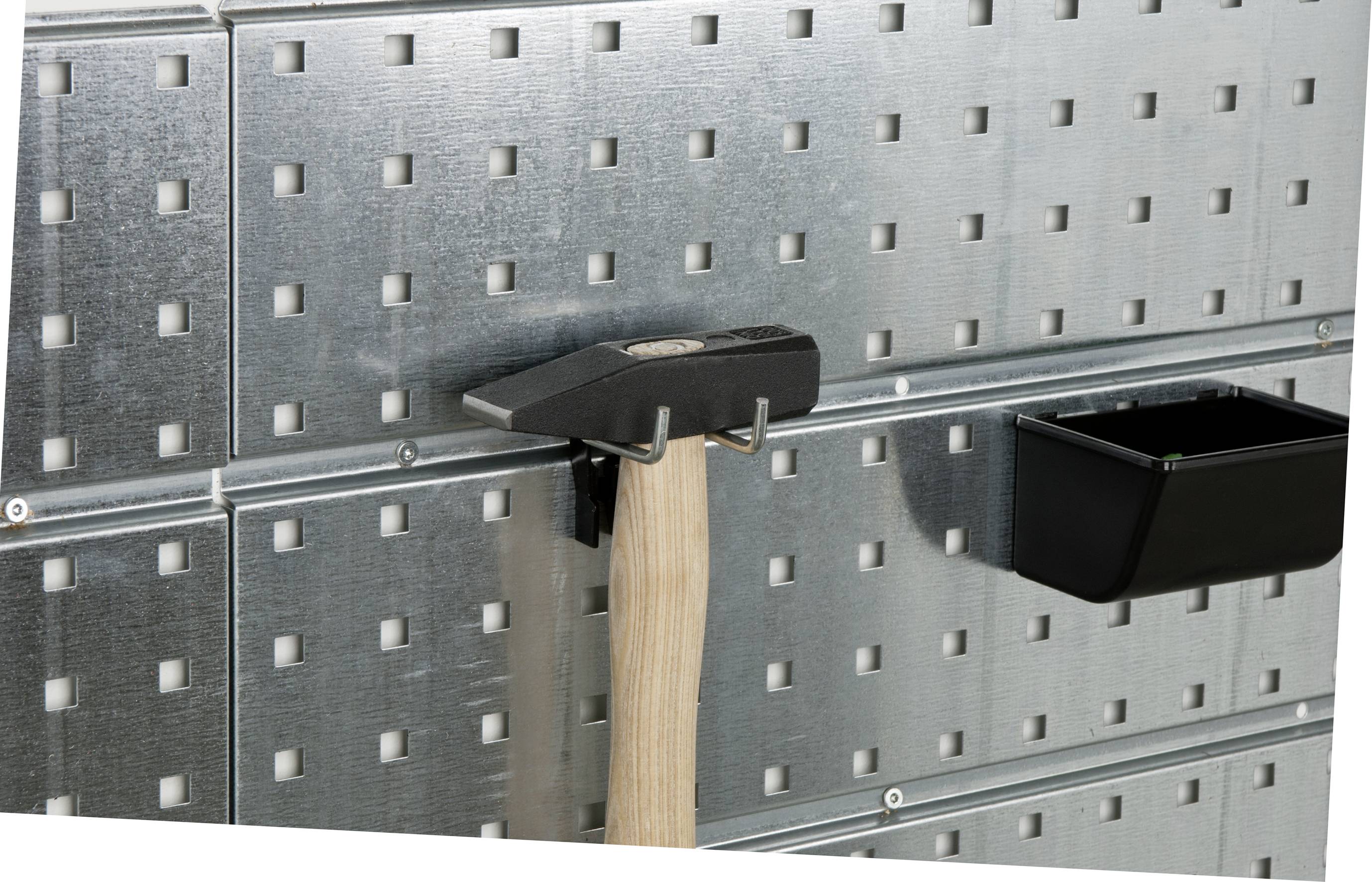 A hammer hangs on a metal wall with square patterns; next to it a small black storage compartment.