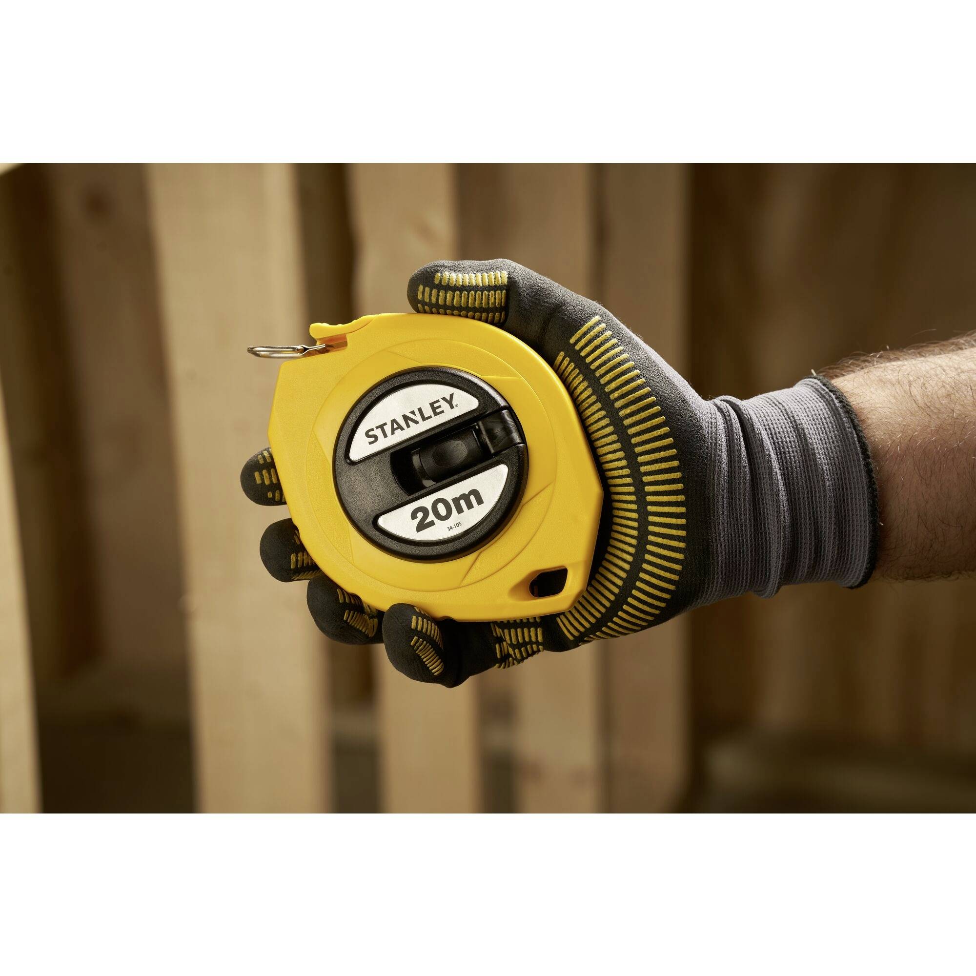 A gloved hand holds a yellow measuring tape with a '20m' marking, with a wooden frame in the background.