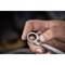 A hand is holding a ring spanner, ready to turn a screw. In the blurred background, a vehicle engine can be seen.