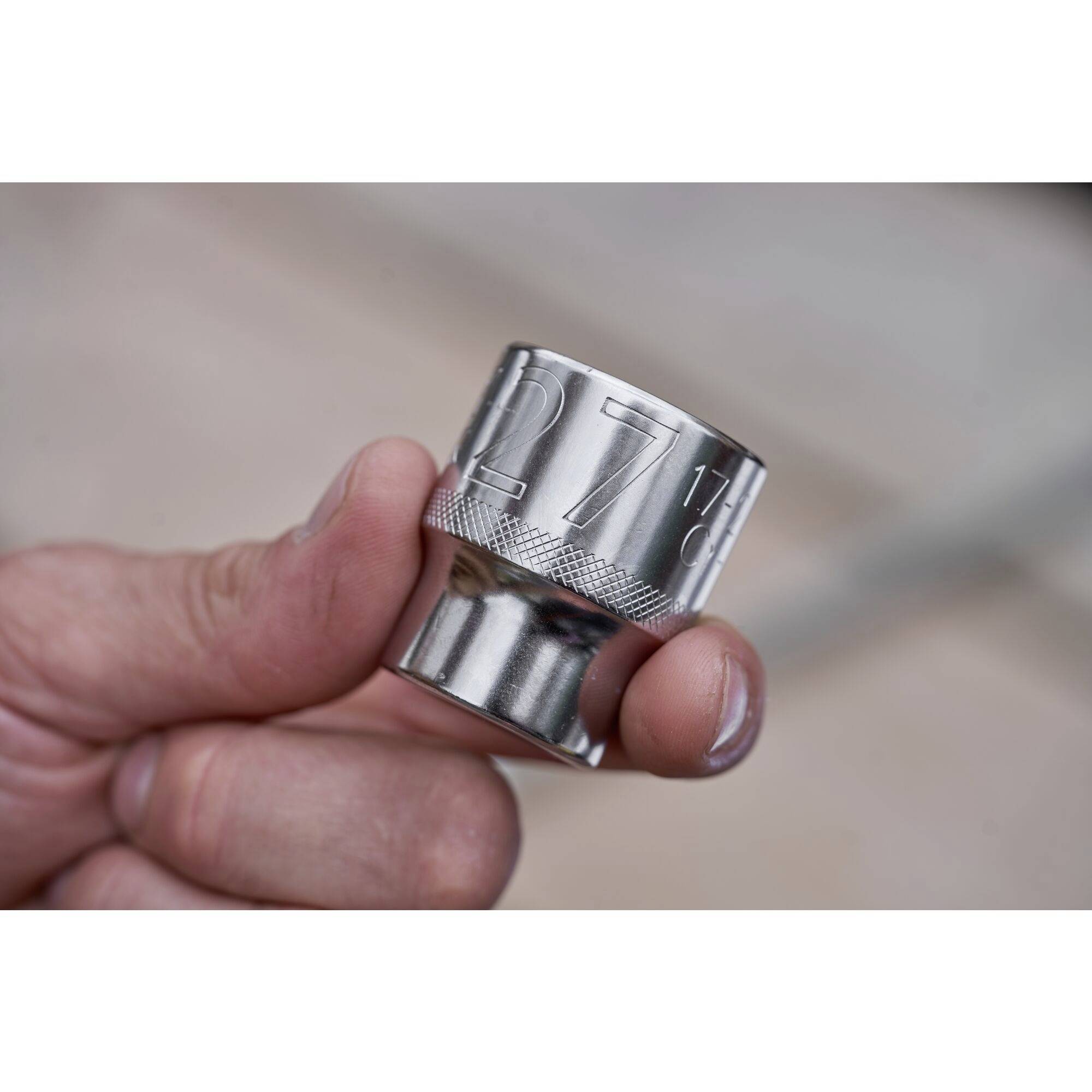 A hand holds a silver socket extension with the number '27' engraved on it, against a blurred background.