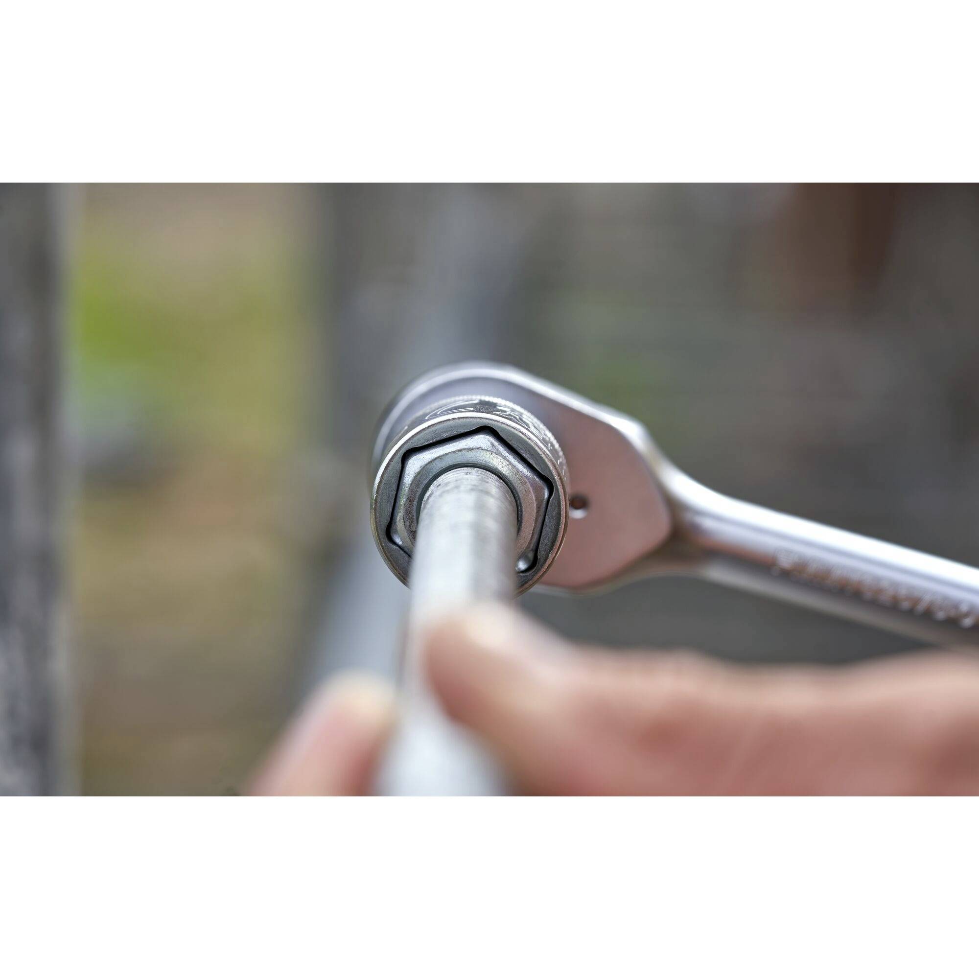 A hand is holding a spanner, tightening a nut on a metal pipe. The focus is on the tool and the connection.