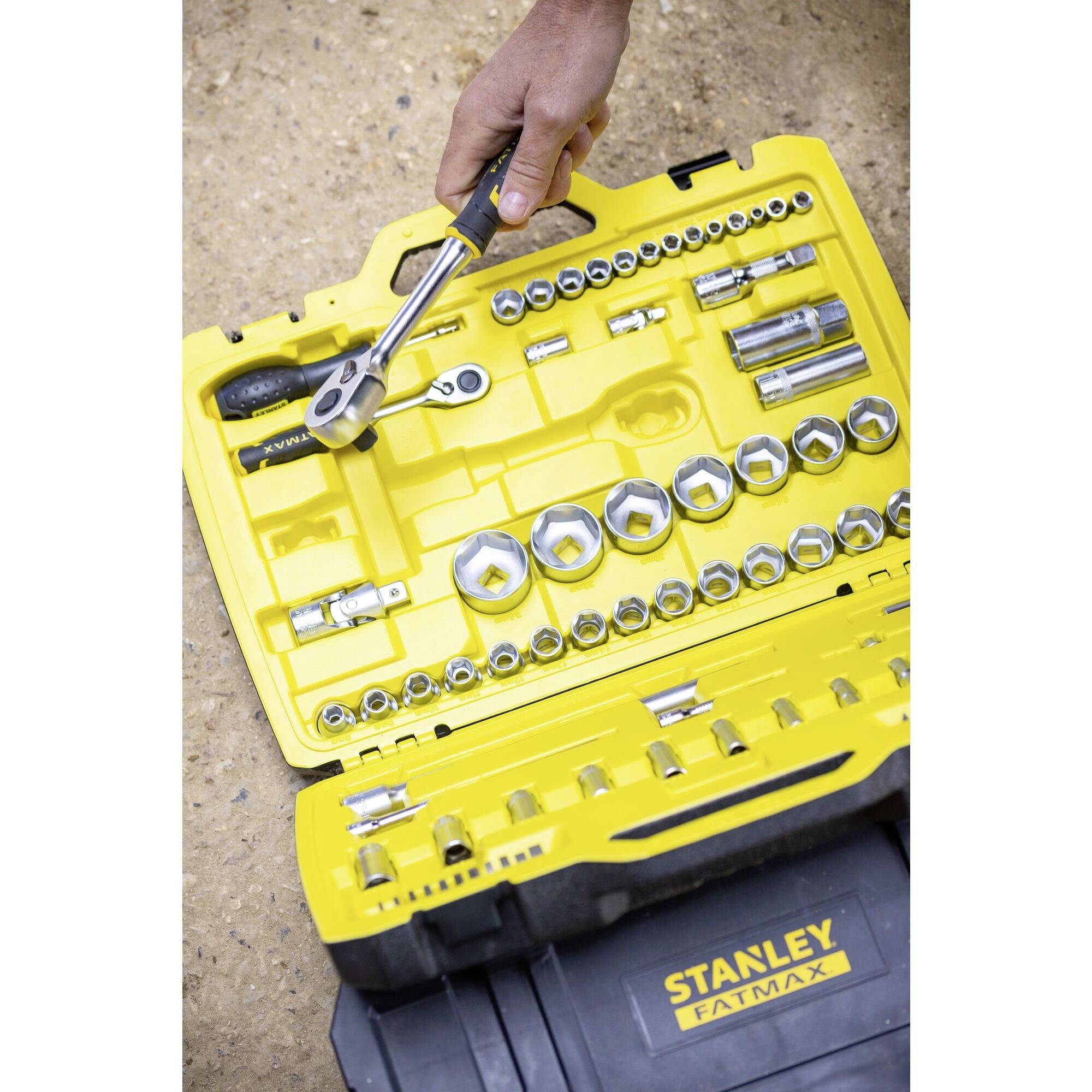 A tool case with a yellow casing displays various socket keys and a ratchet. A hand reaches for a tool.