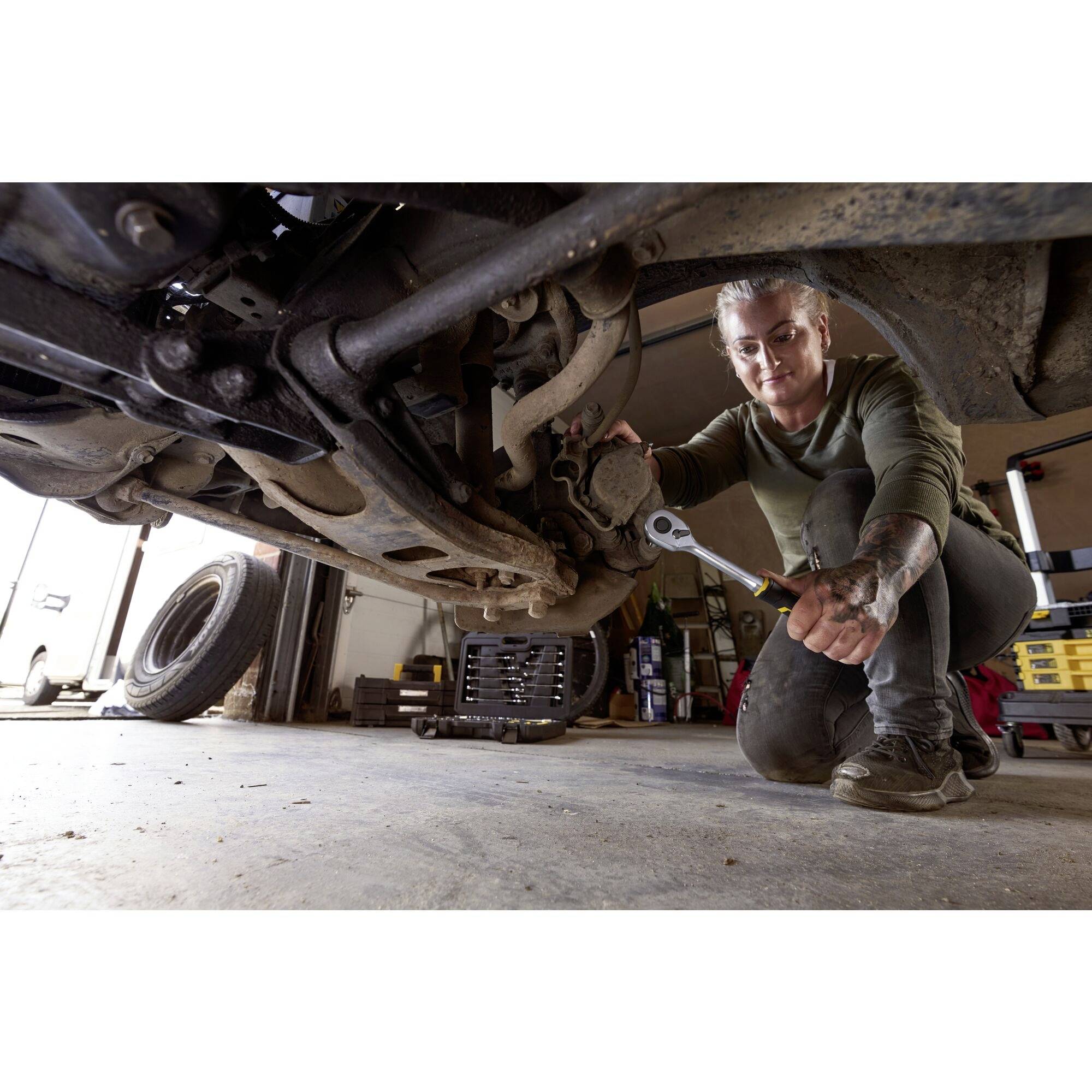 A person is working in a garage underneath a car and using a spanner to repair parts on the chassis.