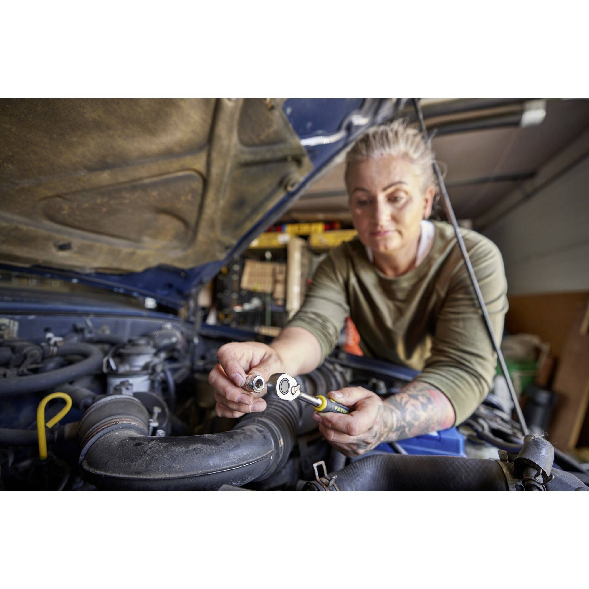 A person is working on a car part in a workshop and using a spanner. Workshop equipment is visible in the background.