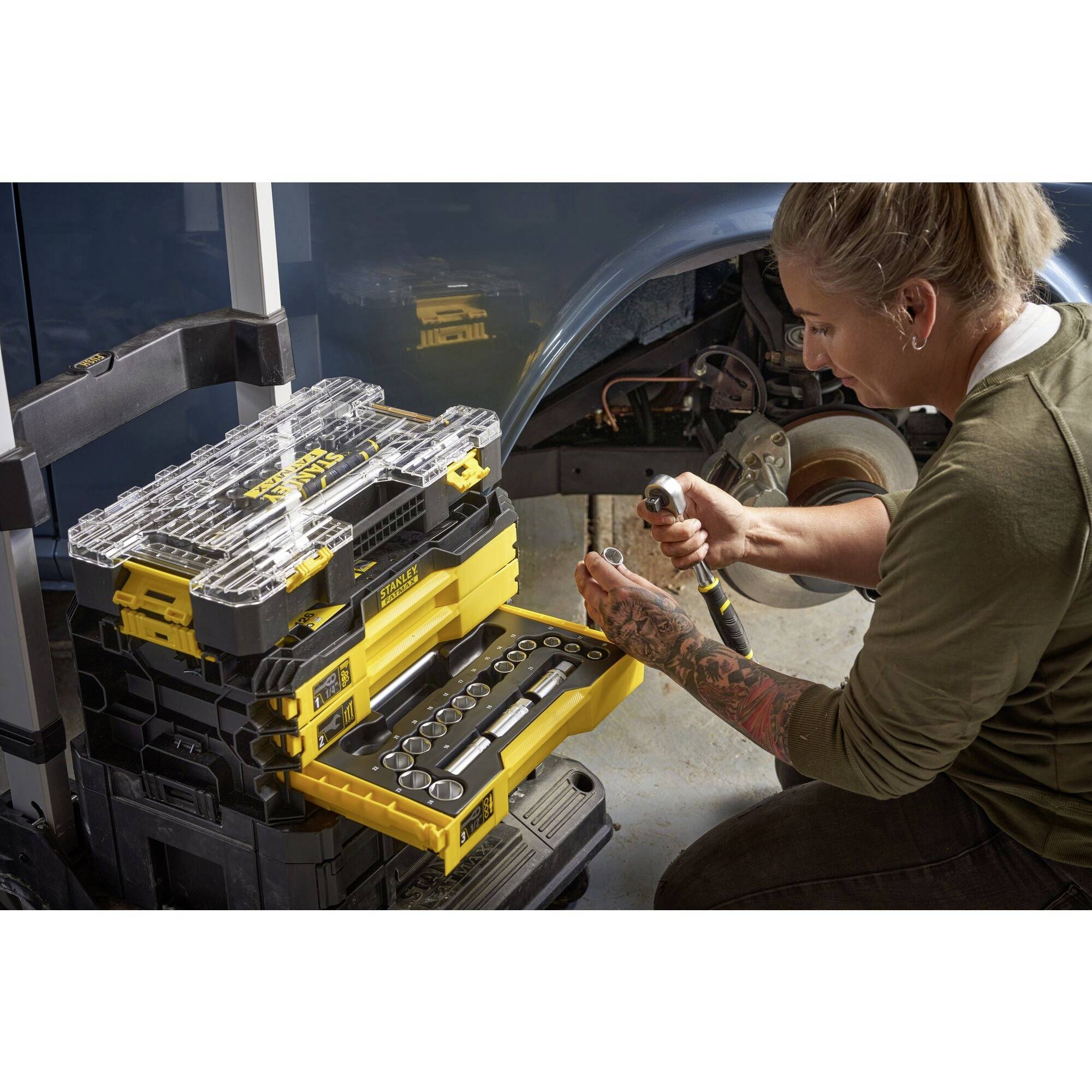 A person is repairing a car and is using a toolbox with open compartments, in which various tools are lying.