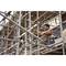 A man is working on a scaffolding with tools. He is focused on a manual task, surrounded by metal struts.