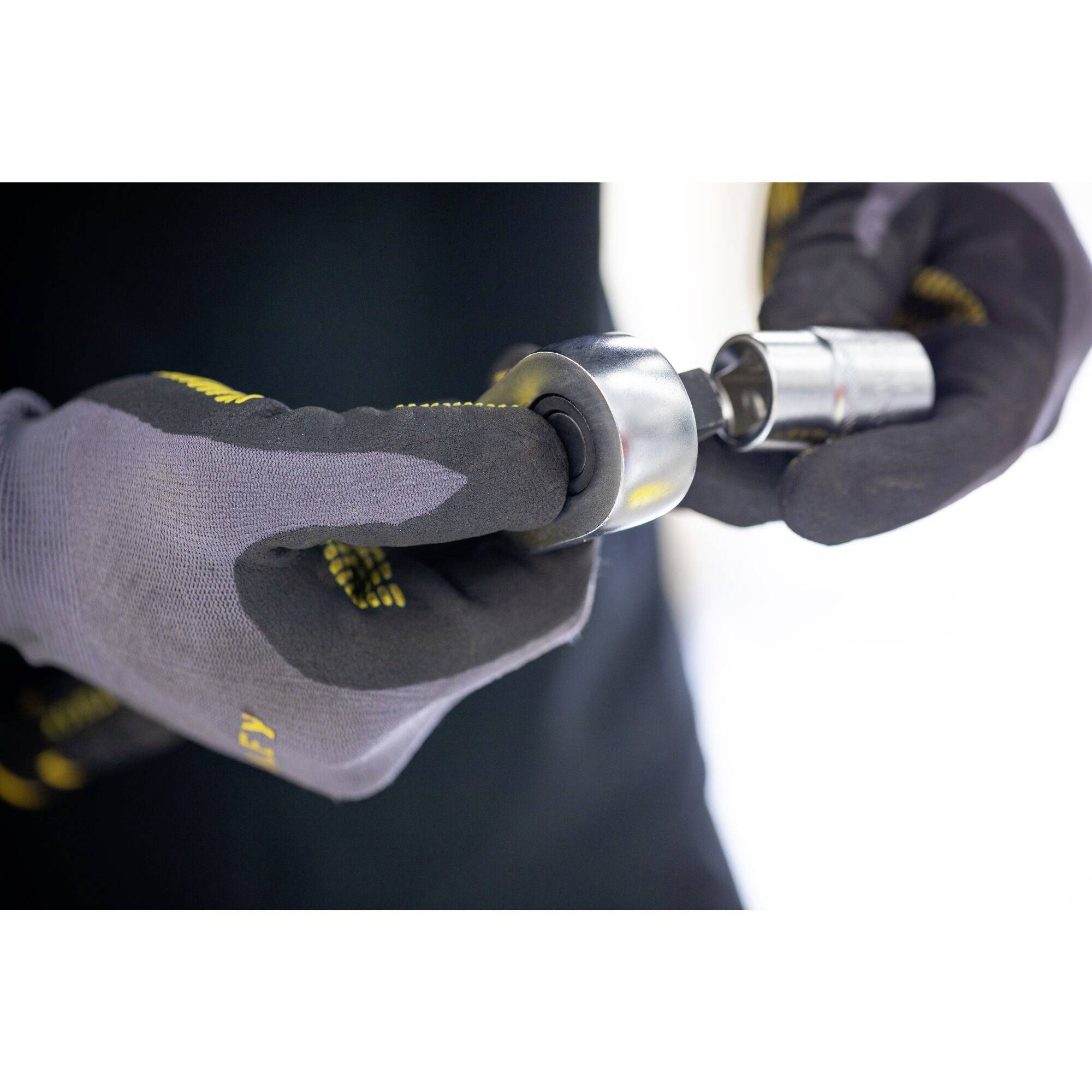 A person is wearing work gloves and holding a silver metal component, possibly a tool part or machine element.