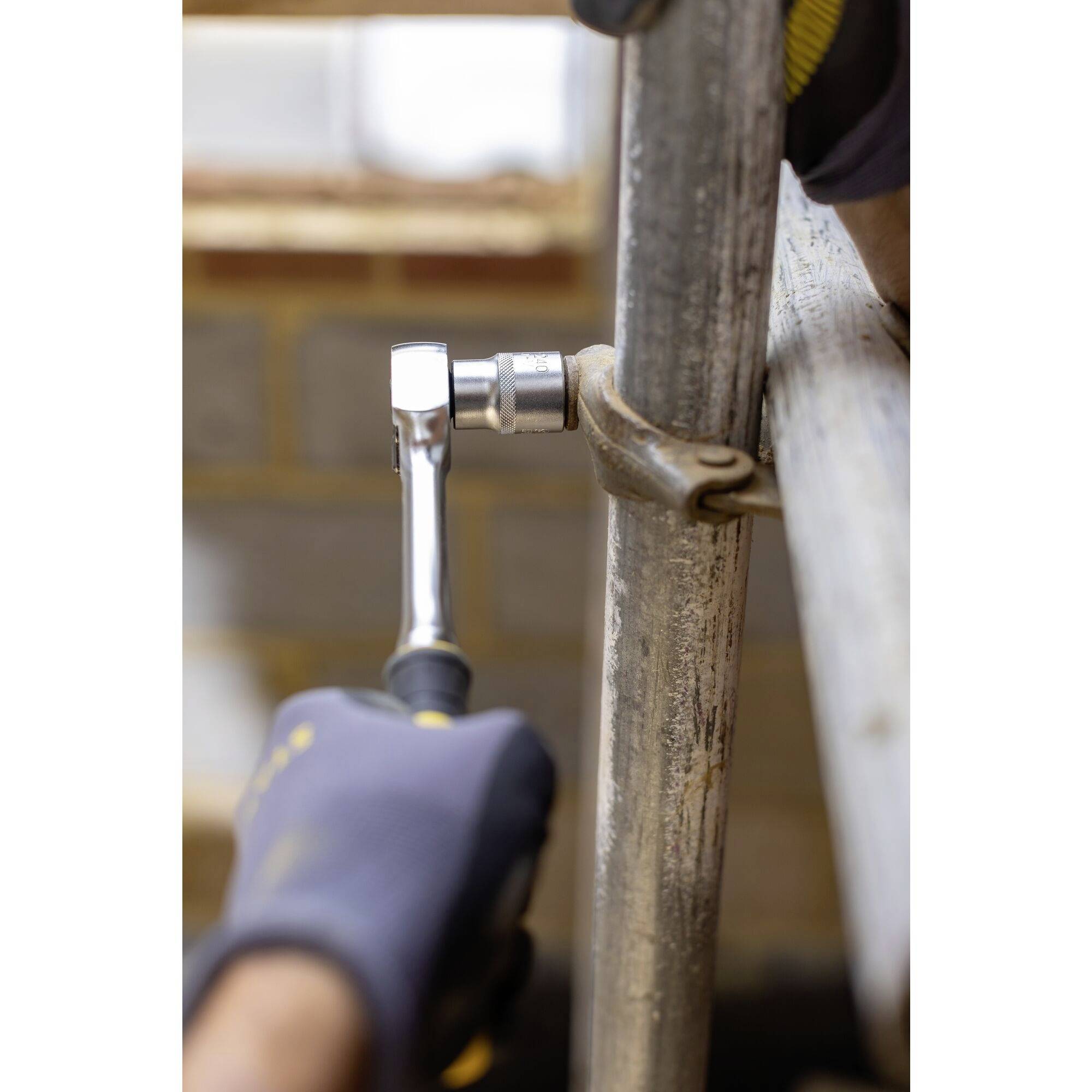 A person wearing gloves is tightening a screw on a metal pipe using a ratchet spanner, with focus on the tool and the task at hand.