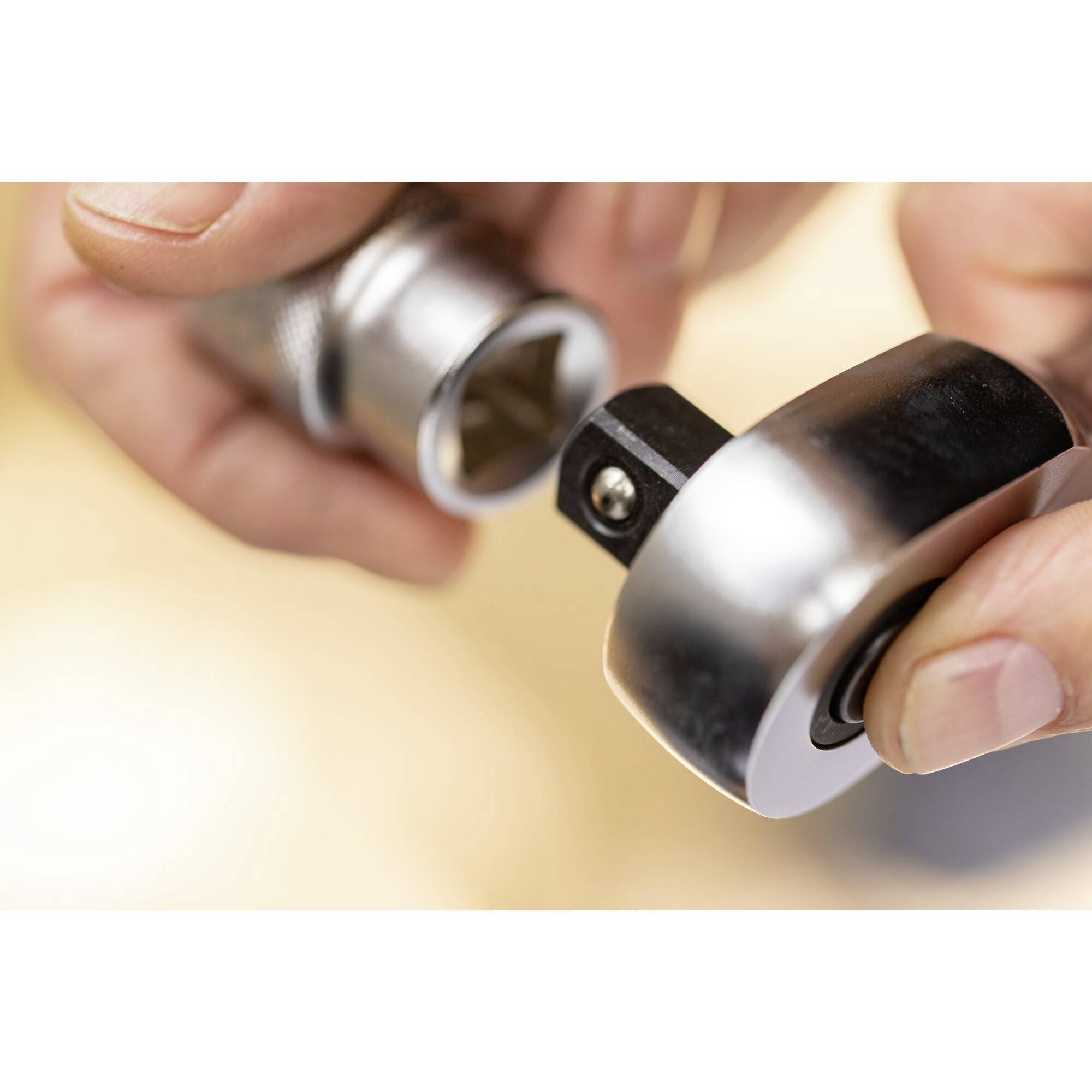 Hands holding a ratchet and attaching a socket insert. Office lighting in the background. Focus on the tool connection.