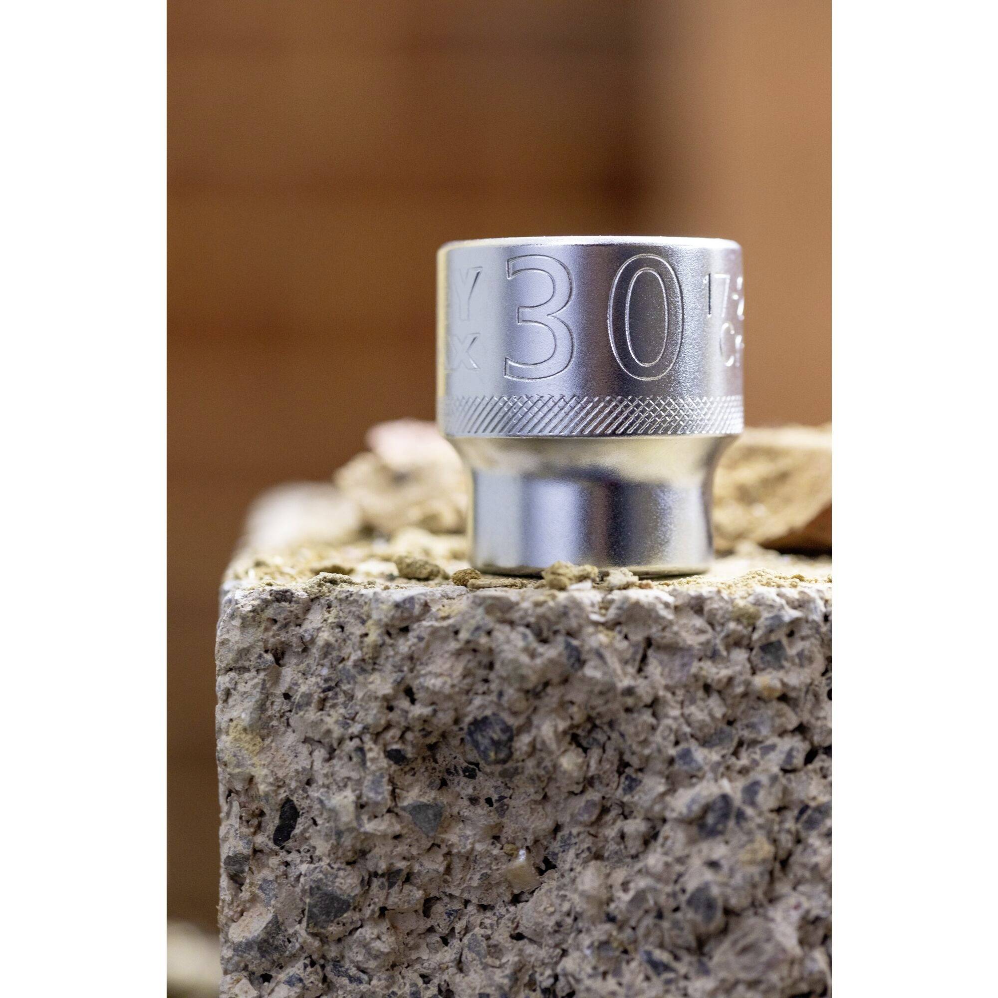 A silver nut with the engraving '30', placed on a rough, stony background.