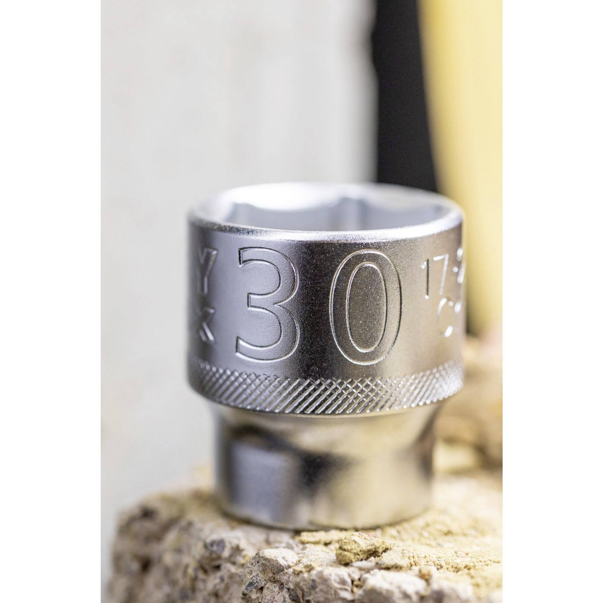 A silver pin badge with the inscription '30' sits on a stone. The background is blurred.