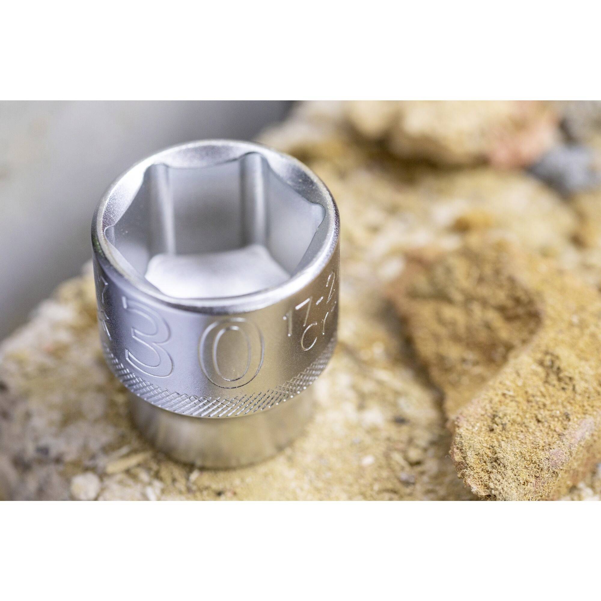 A metal socket lies on sandy ground. It has a hexagonal opening and is rotated so that the size 30 is visible.