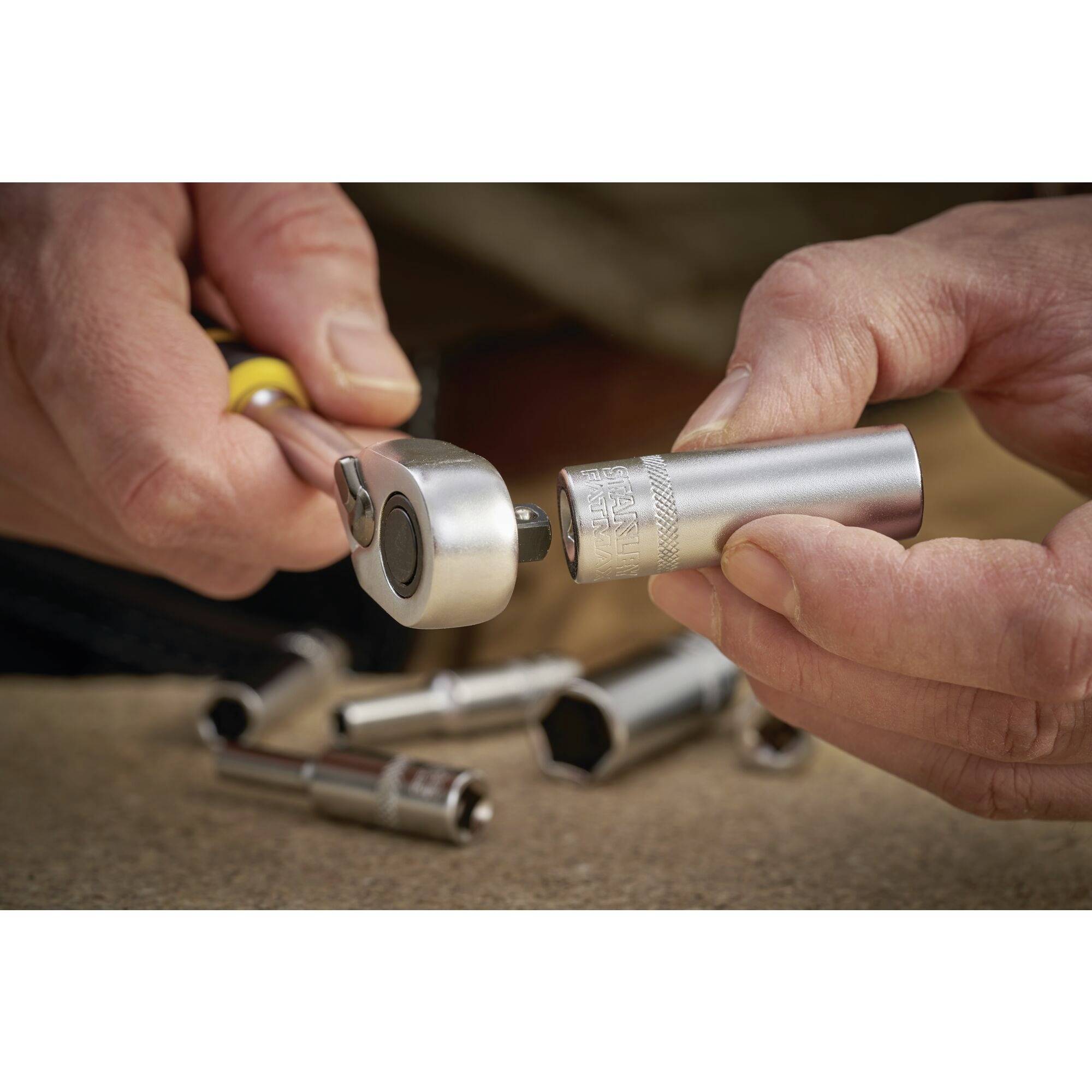 A person is holding and using a socket wrench set to turn a screw. Several sockets are lying in the background.