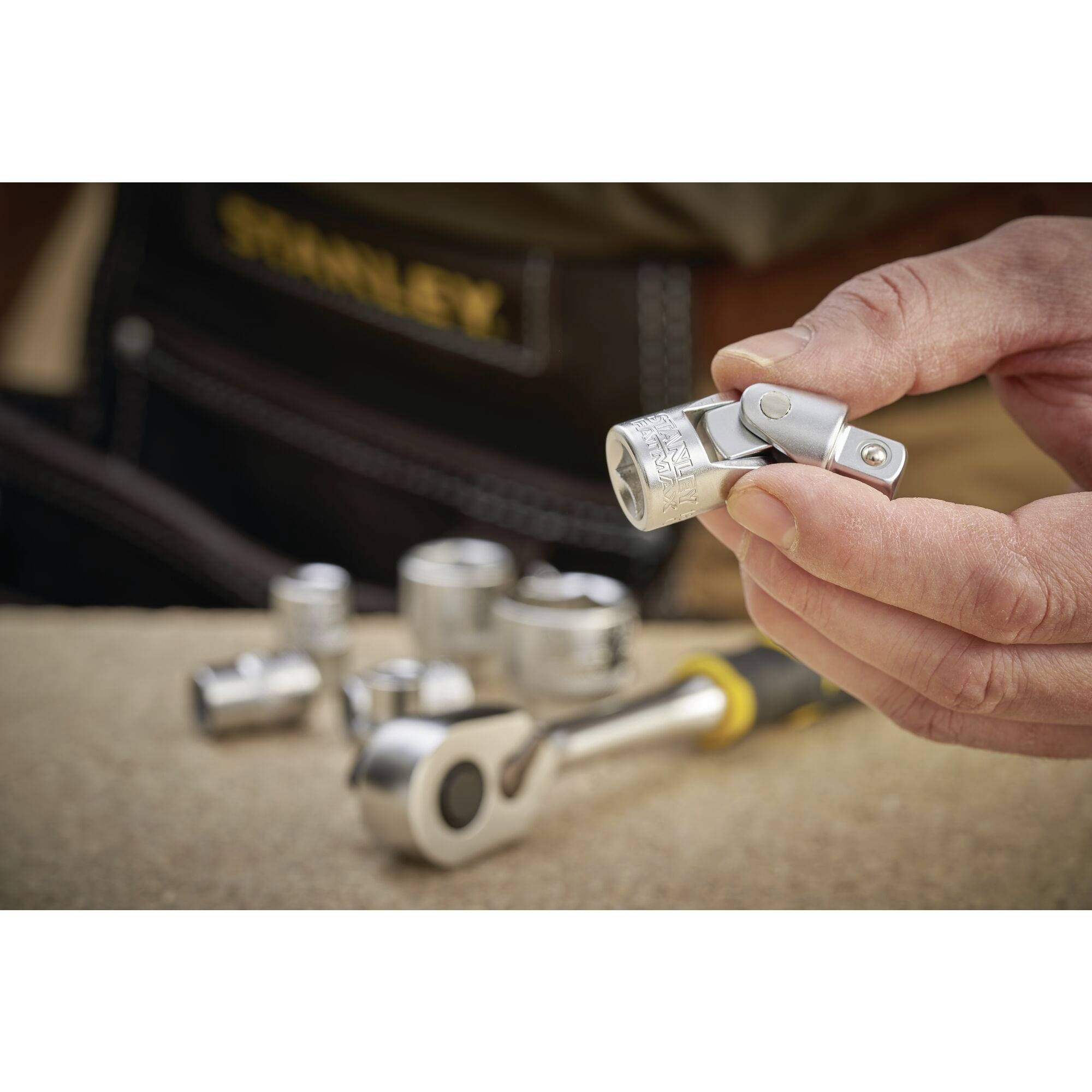 A hand is holding a square drive socket adaptor, surrounded by blurred sockets and a ratchet on a workbench.