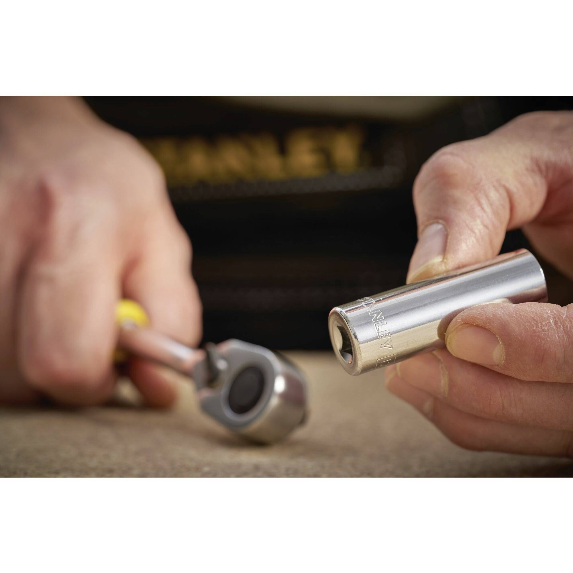 A hand is holding a silver hexagonal nut, while the other hand grips a ratchet spanner. They are preparing to use the tool.