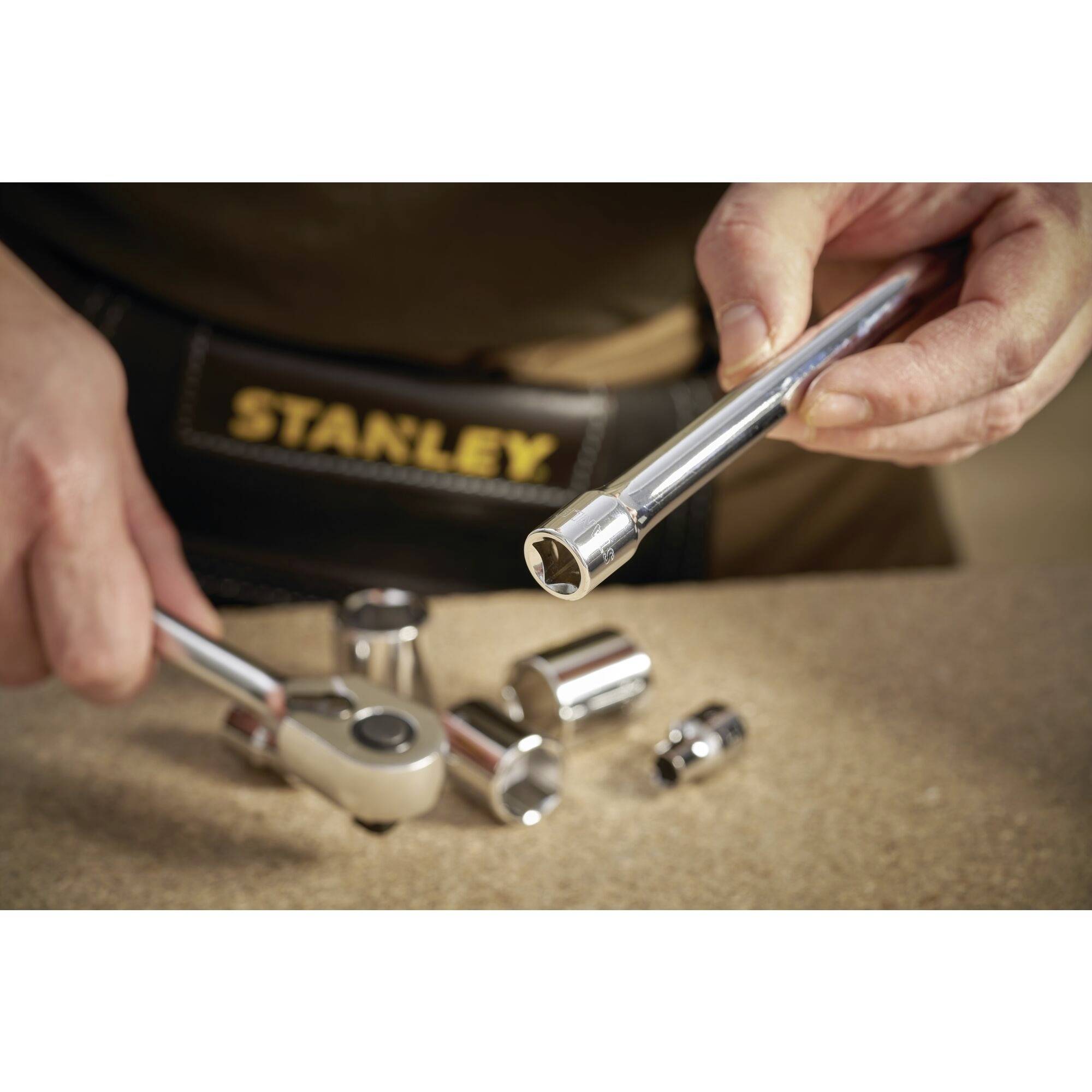 A person is pointing at a socket spanner with a shifting spanner. A tool bag is visible in the background.