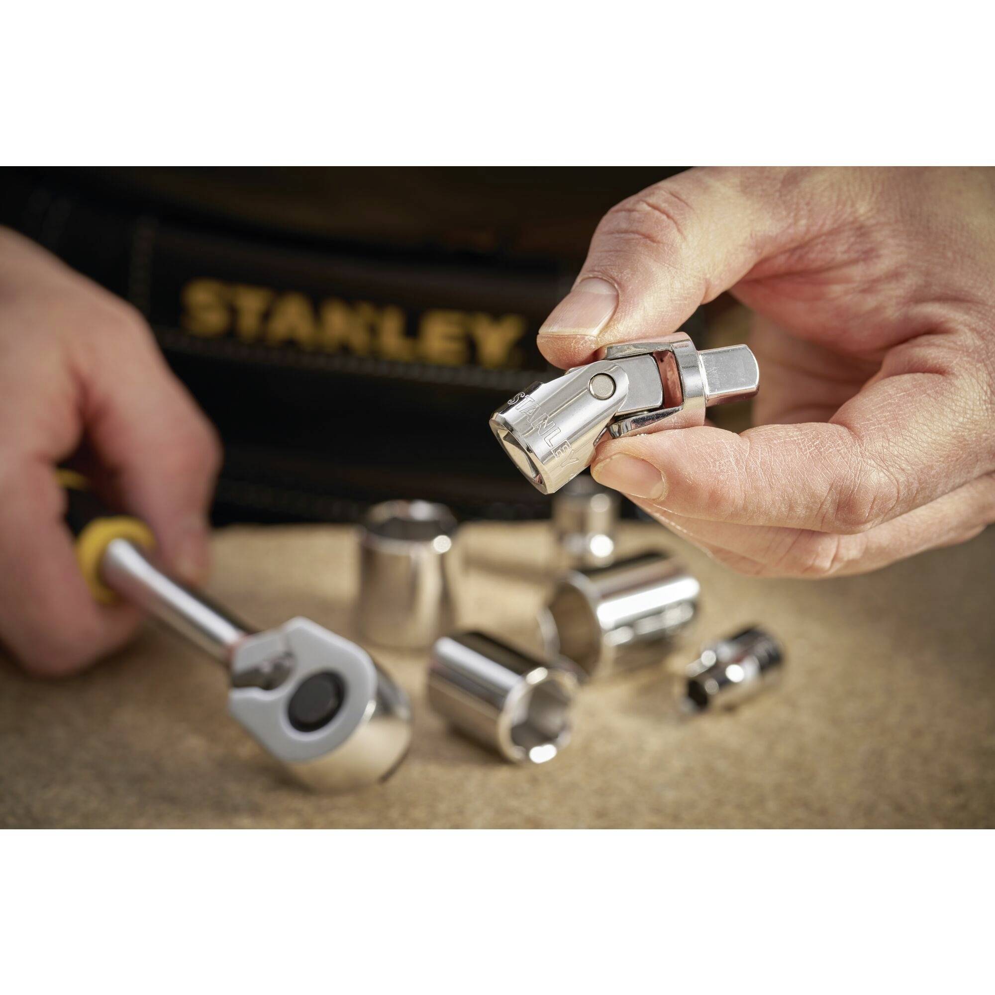 A hand is holding a socket, which belongs to a socket wrench set. In the background, additional sockets and a tool case are visible.