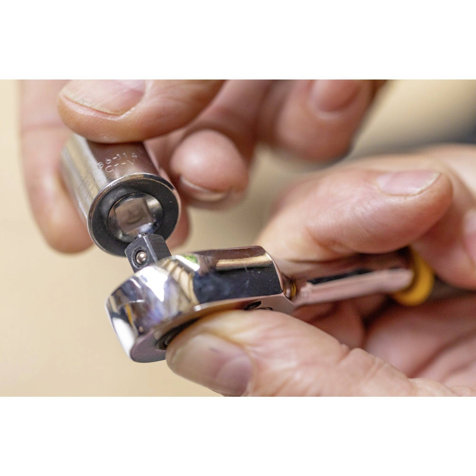 A hand is holding a ratchet spanner with a socket. The focus is on close-up tool usage.