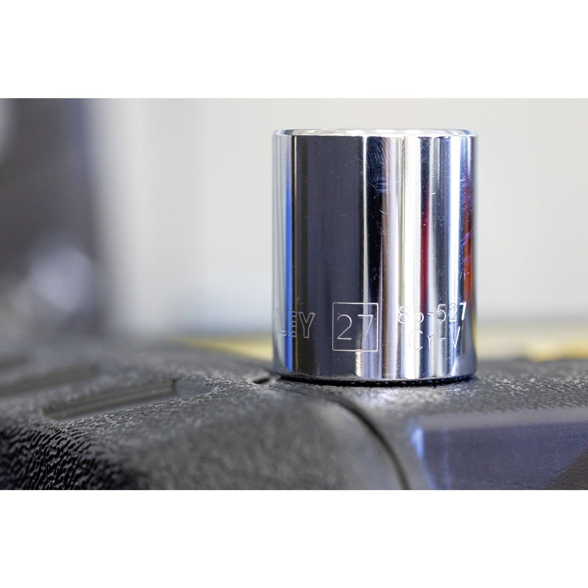 A gleaming socket wrench in close-up on a toolbox, with the inscription '27 mm' clearly visible on the surface.