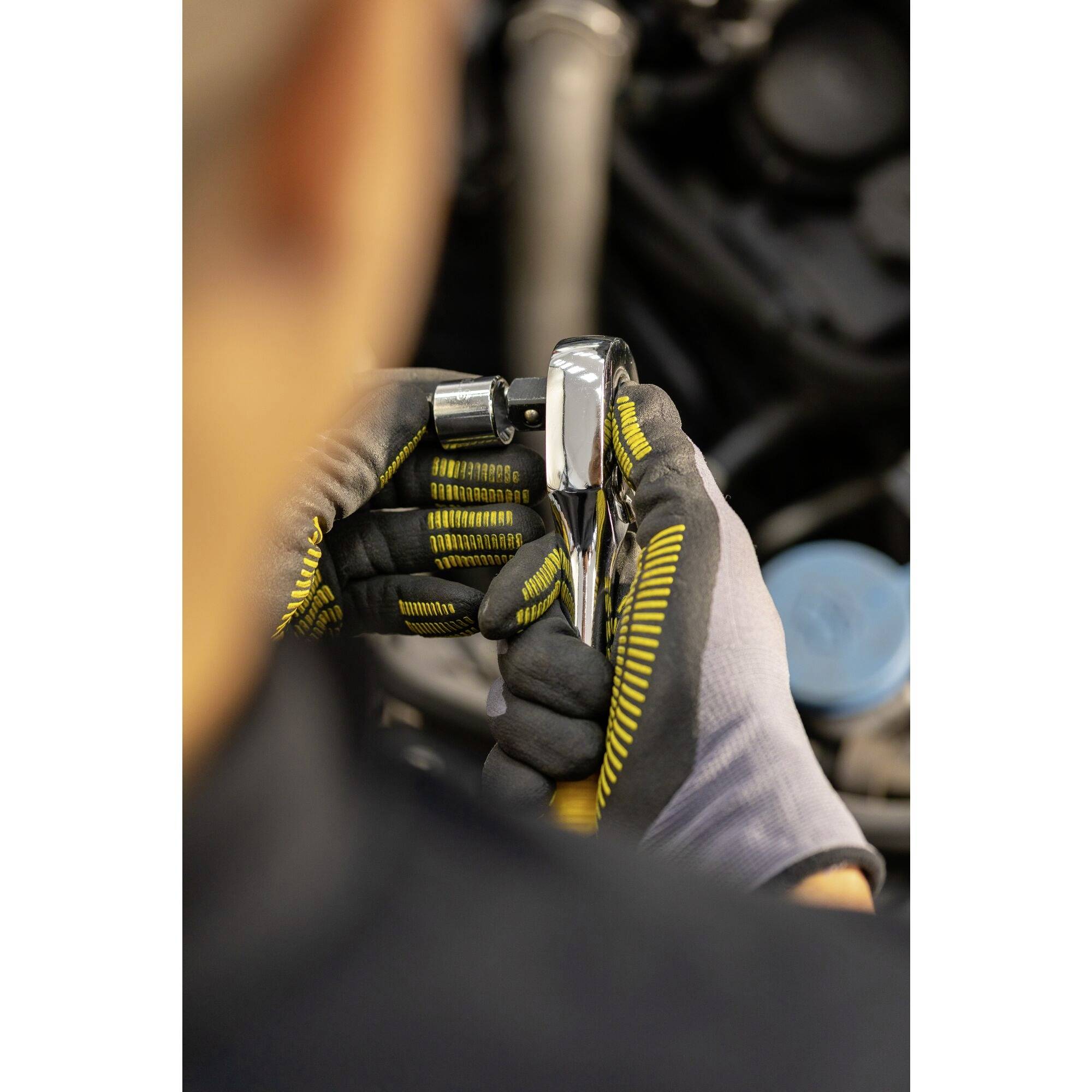 A person wearing work gloves is using a spanner to work on a vehicle engine.
