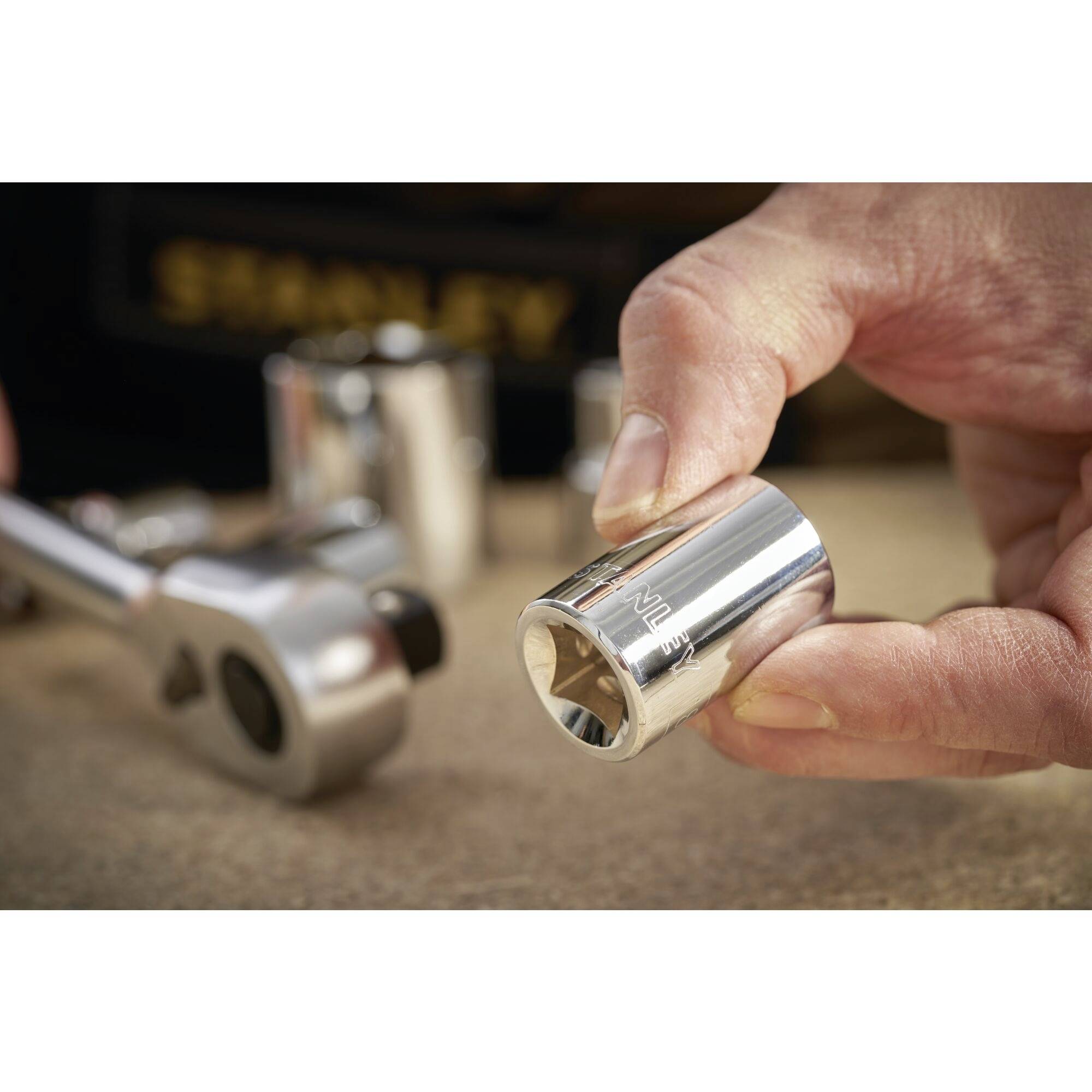 A hand holds a shiny dowel pin over a workbench, with additional tools lying in the background.