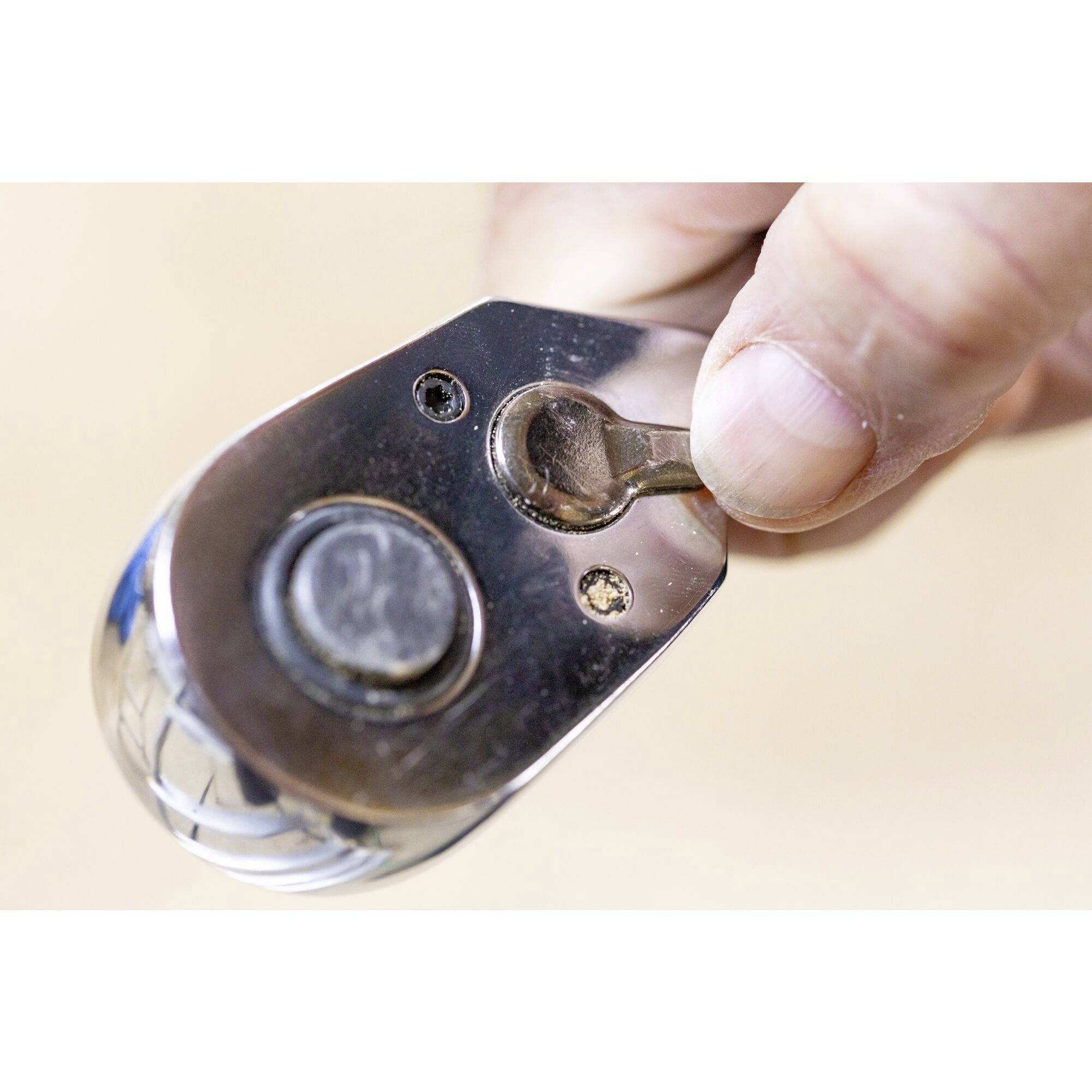 A hand holds a chrome-plated ratchet tool with a rotating mechanism in close-up.