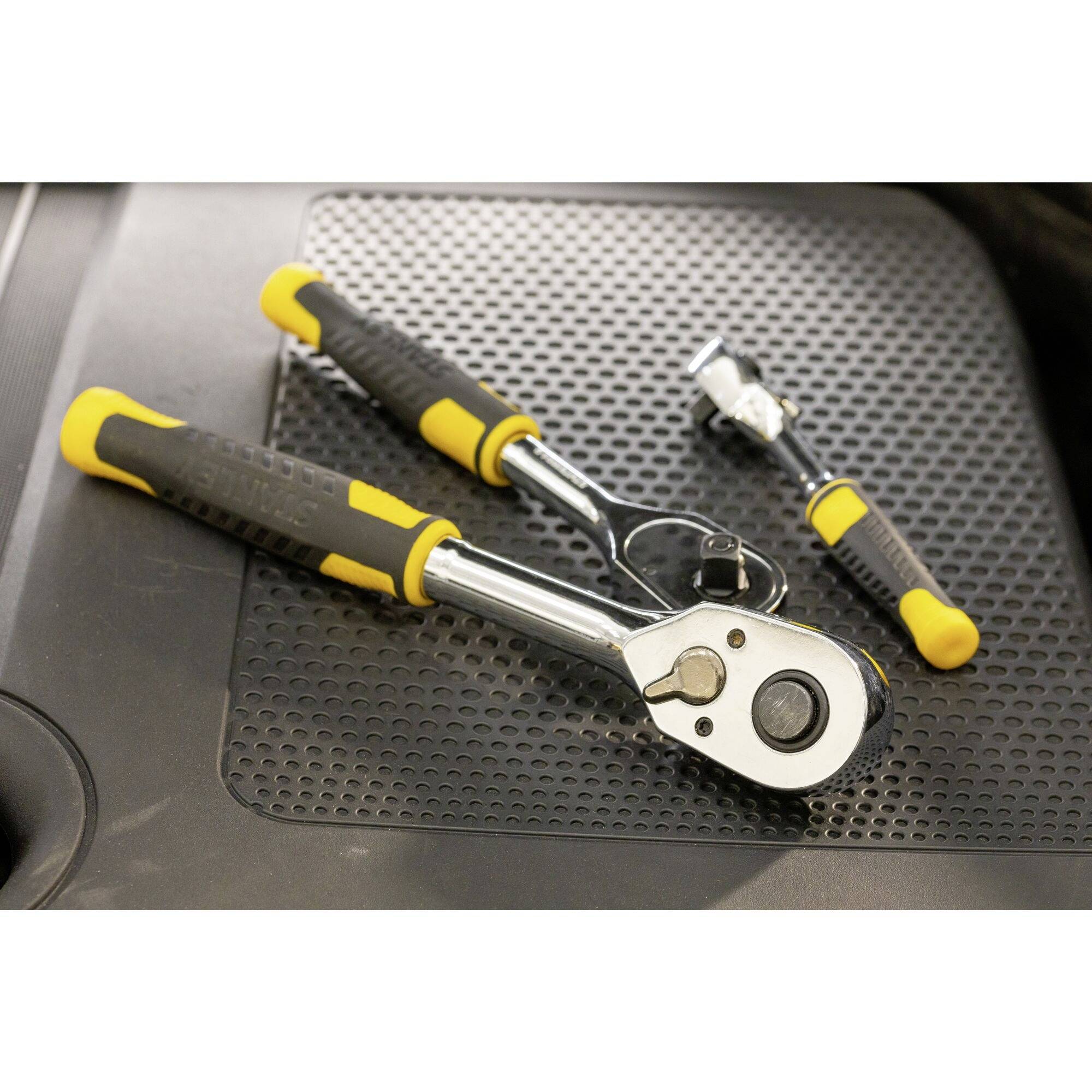 Two ratchets with yellow and black handles are lying on a non-slip mat.