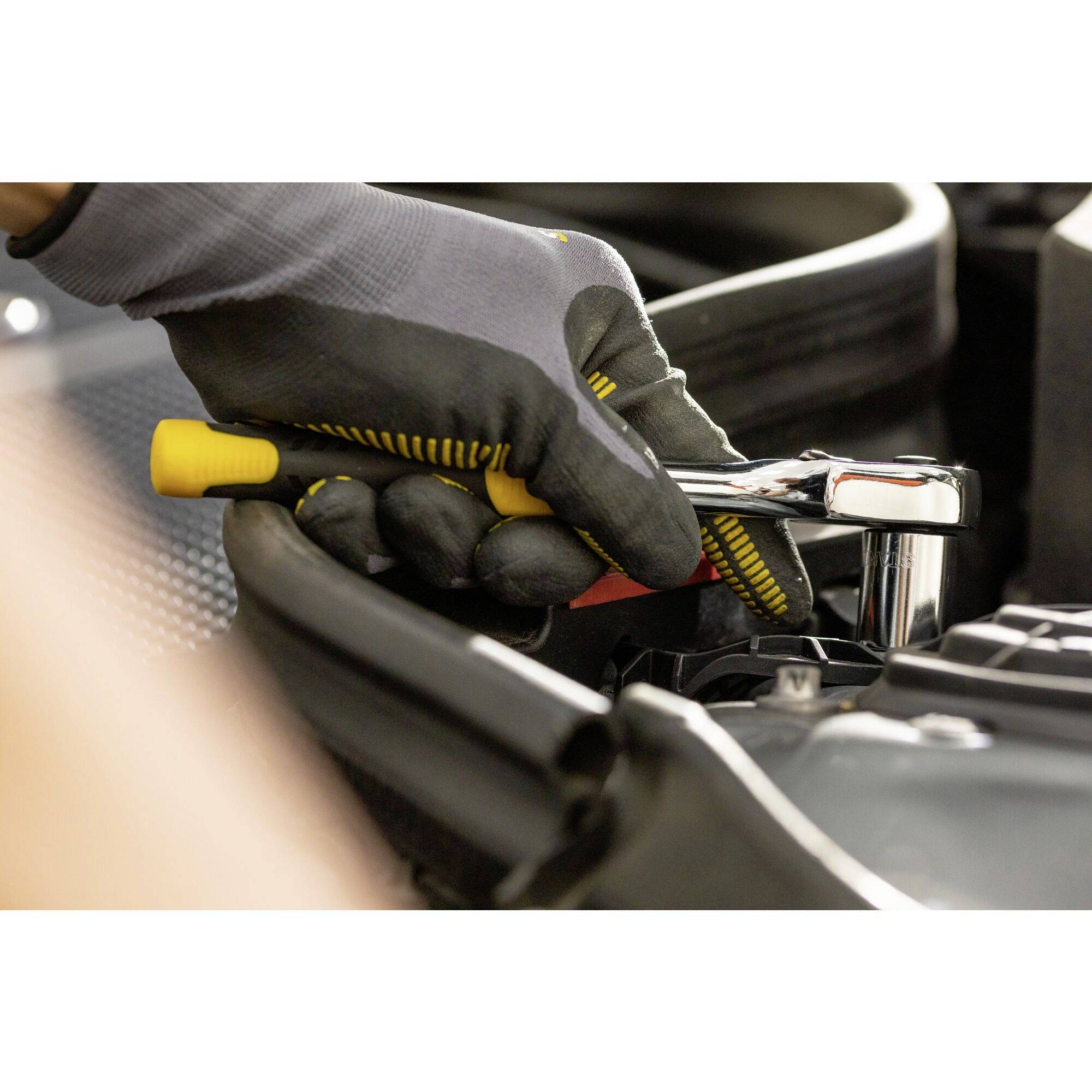 A person wearing gloves repairs an engine with a spanner. The focus is on the tool and the hand.
