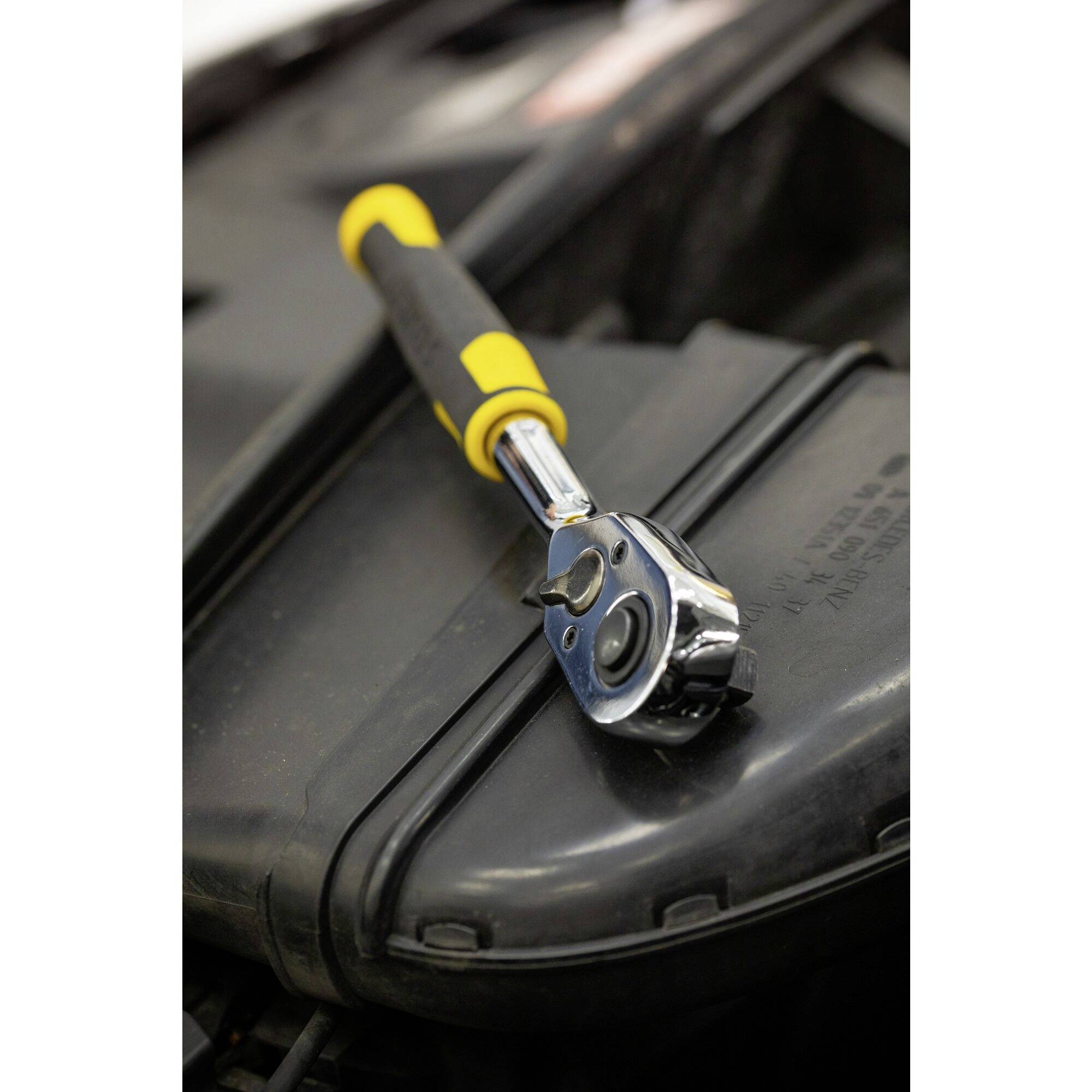 A spanner with a yellow handle is lying on the black engine component of a vehicle.